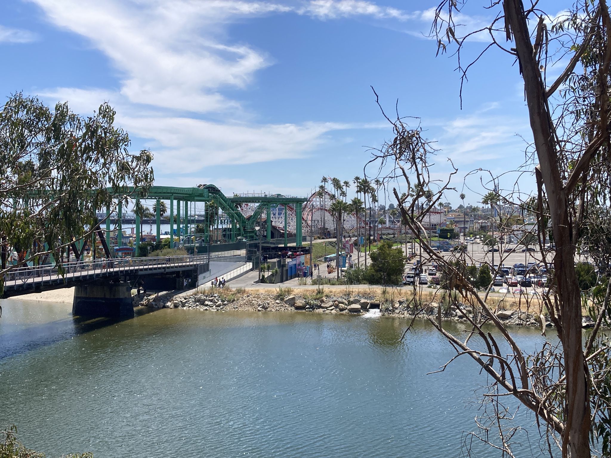 Green truss bridge spans water, with a city and palm trees under a sunny sky. - Old Santa Cruz Highway – Schwan Lake loop from Beach Station (Santa Cruz)