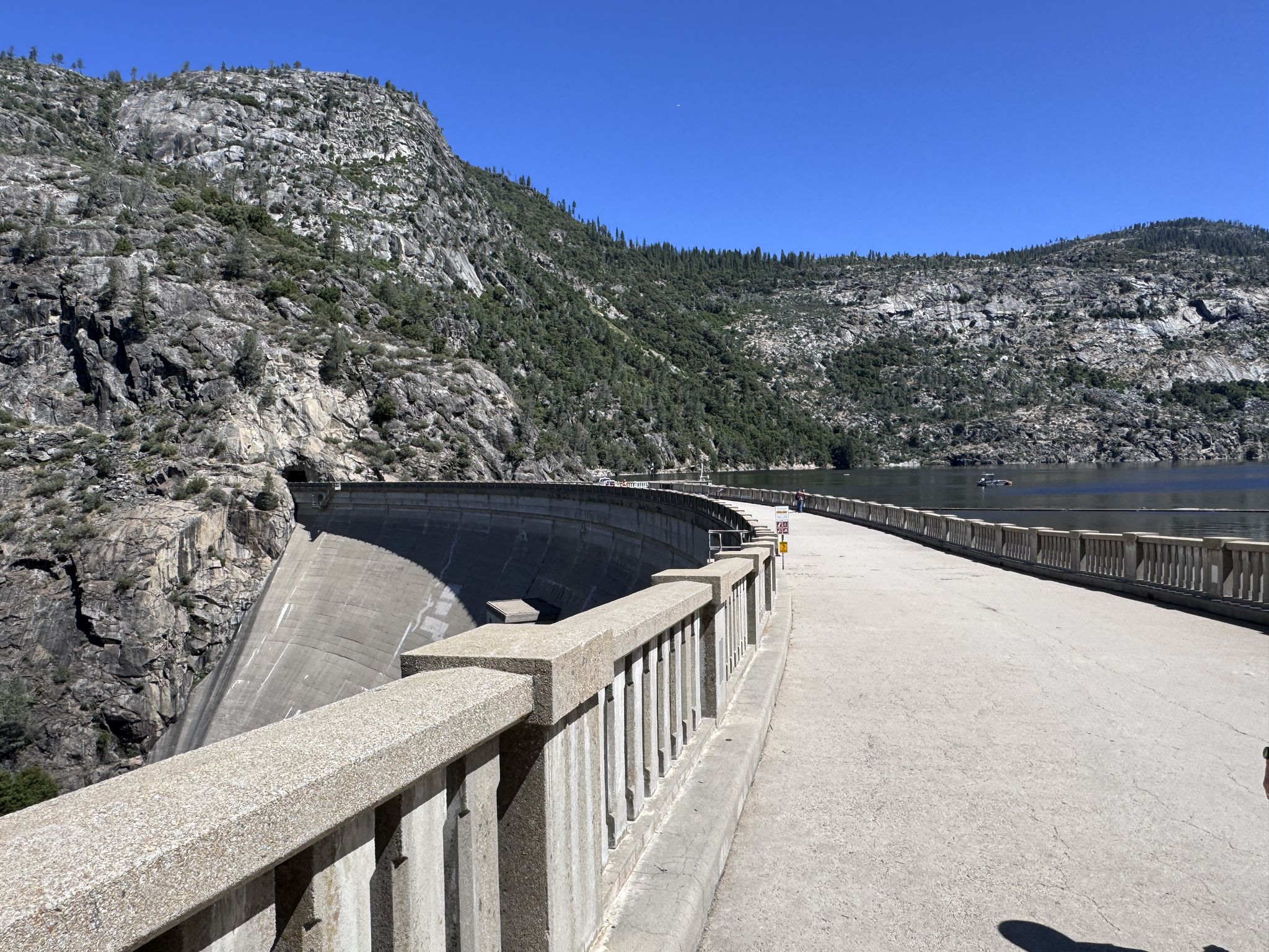 A large curved concrete dam under bright sun, with rocky mountains and water. - Mather to Hetch Hetchy Reservoir