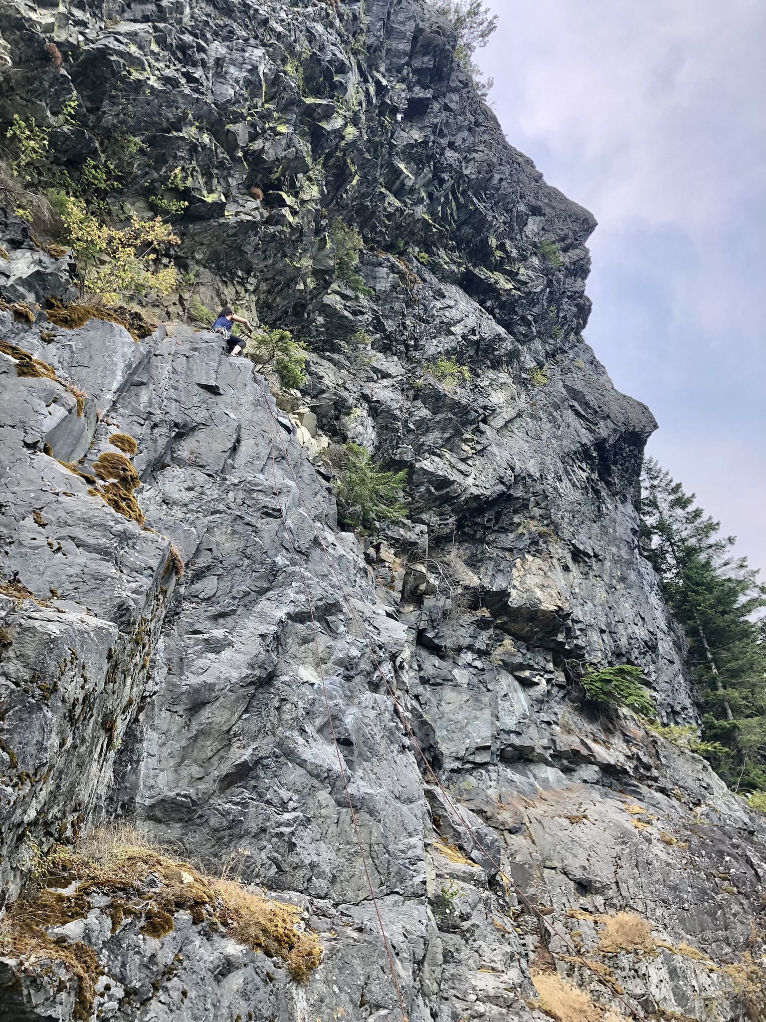 Person on a steep, rugged rock cliff face under an overcast sky. - Change Creek Trestle – Hall Creek Trestle loop from Olallie State Park South Fork Fishing Access