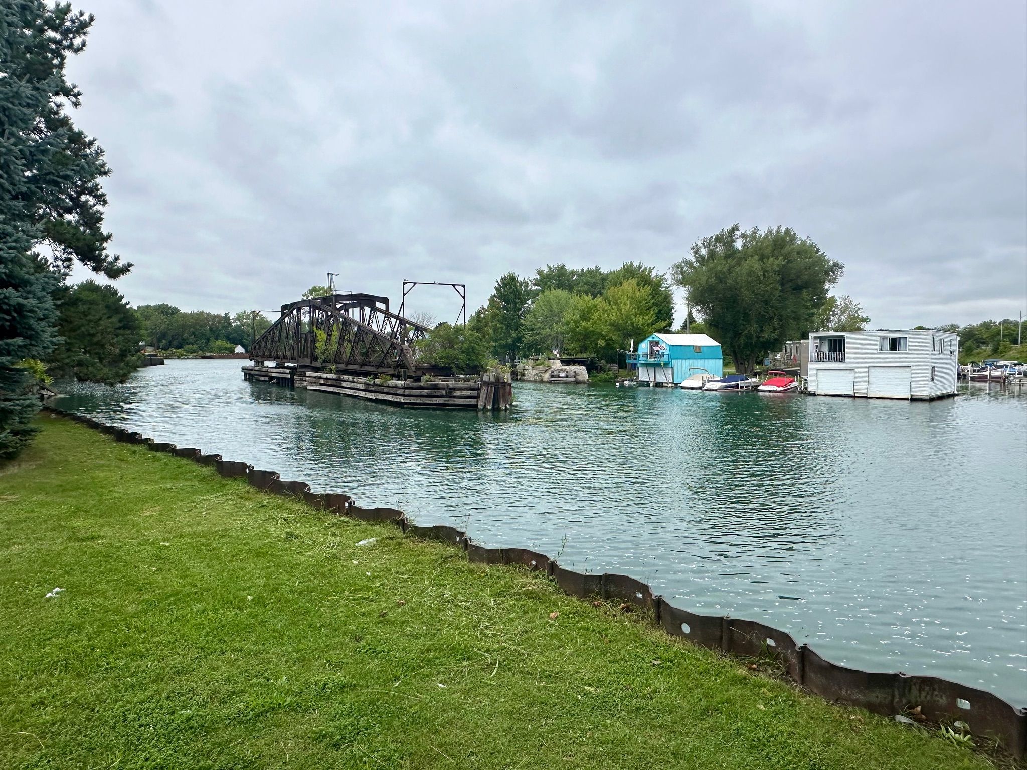 A waterway with a swing bridge, houses, and boats under a cloudy sky. - Tonawanda Rail Trail (Buffalo to Tonawanda)