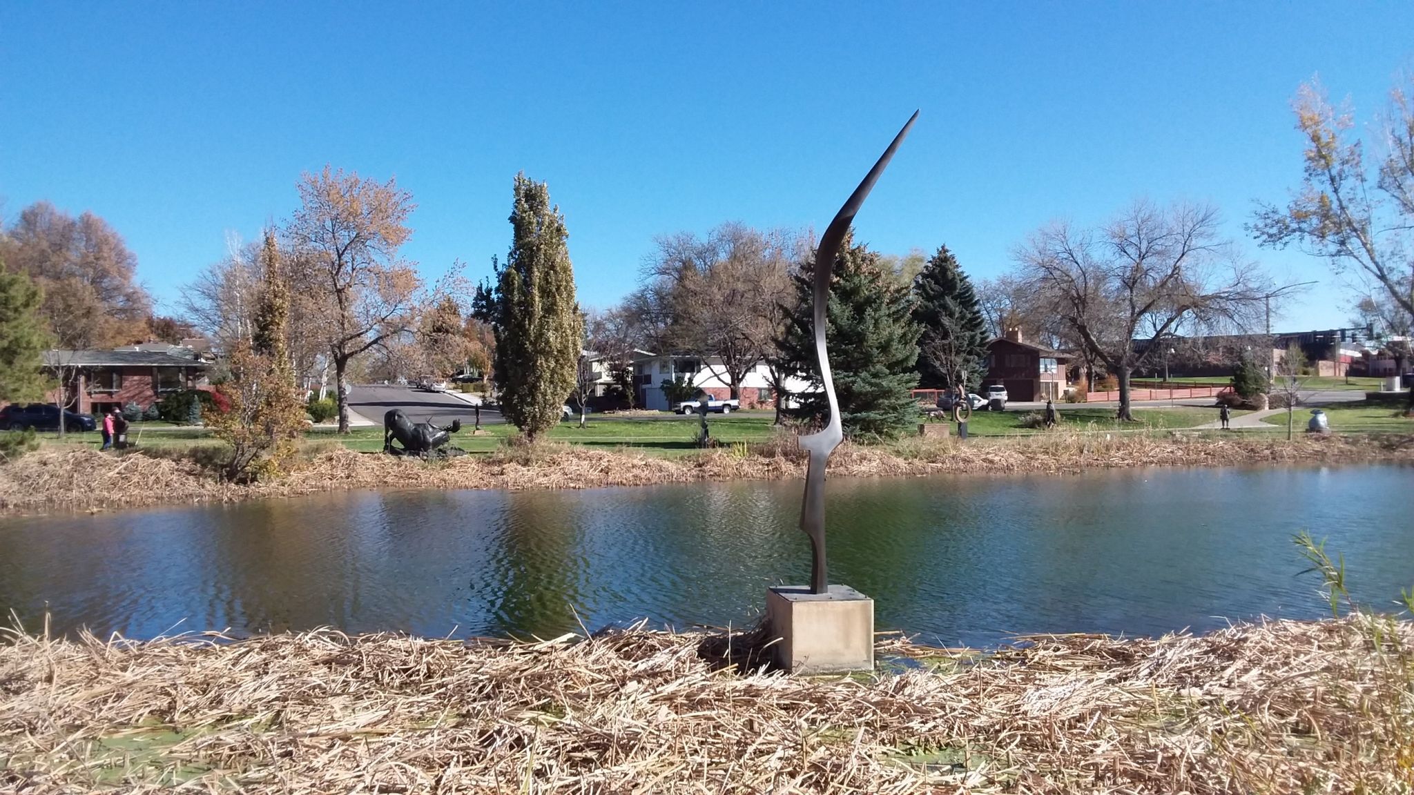 Abstract metal sculpture next to a calm pond under a clear sky. - Benson Sculpture Garden Trail