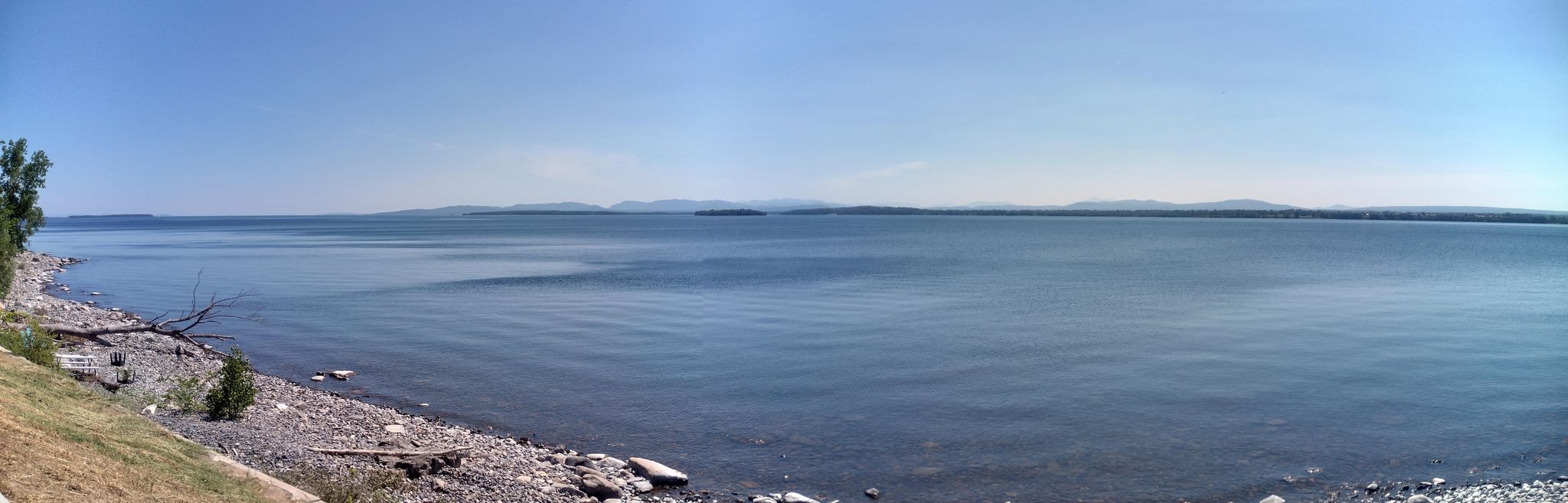 Panoramic view of a calm lake with a rocky shore on a sunny day. - Downtown Plattsburg – Champlain Valley Trail loop from Treadwell Bay Marina & Resort