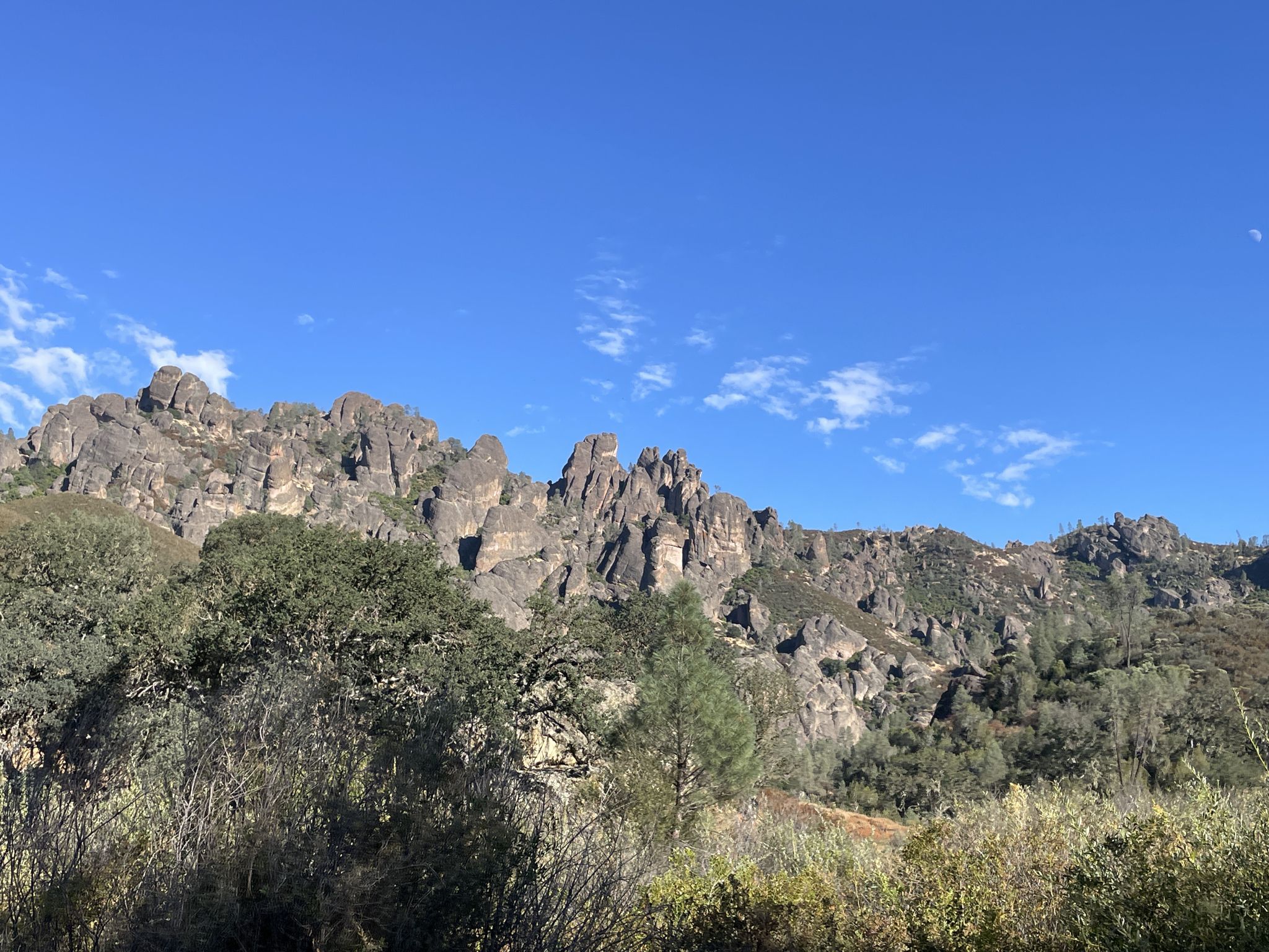 Sunlit rocky peaks and green foliage against a bright blue sky. - North Wilderness Trail to Twin Knolls