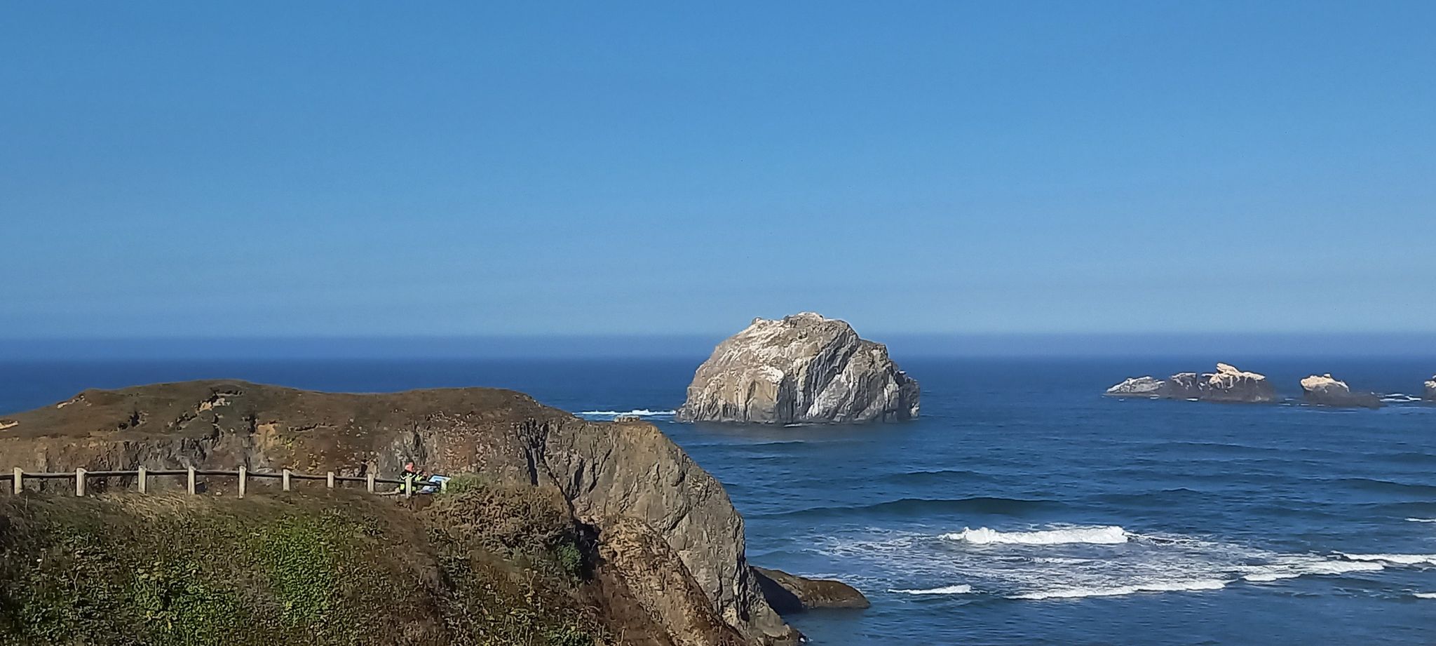 Sunny coastal cliff overlooking a large rock formation in the deep blue ocean. - Bandon loop via Oregon Coast Scenic Bikeway
