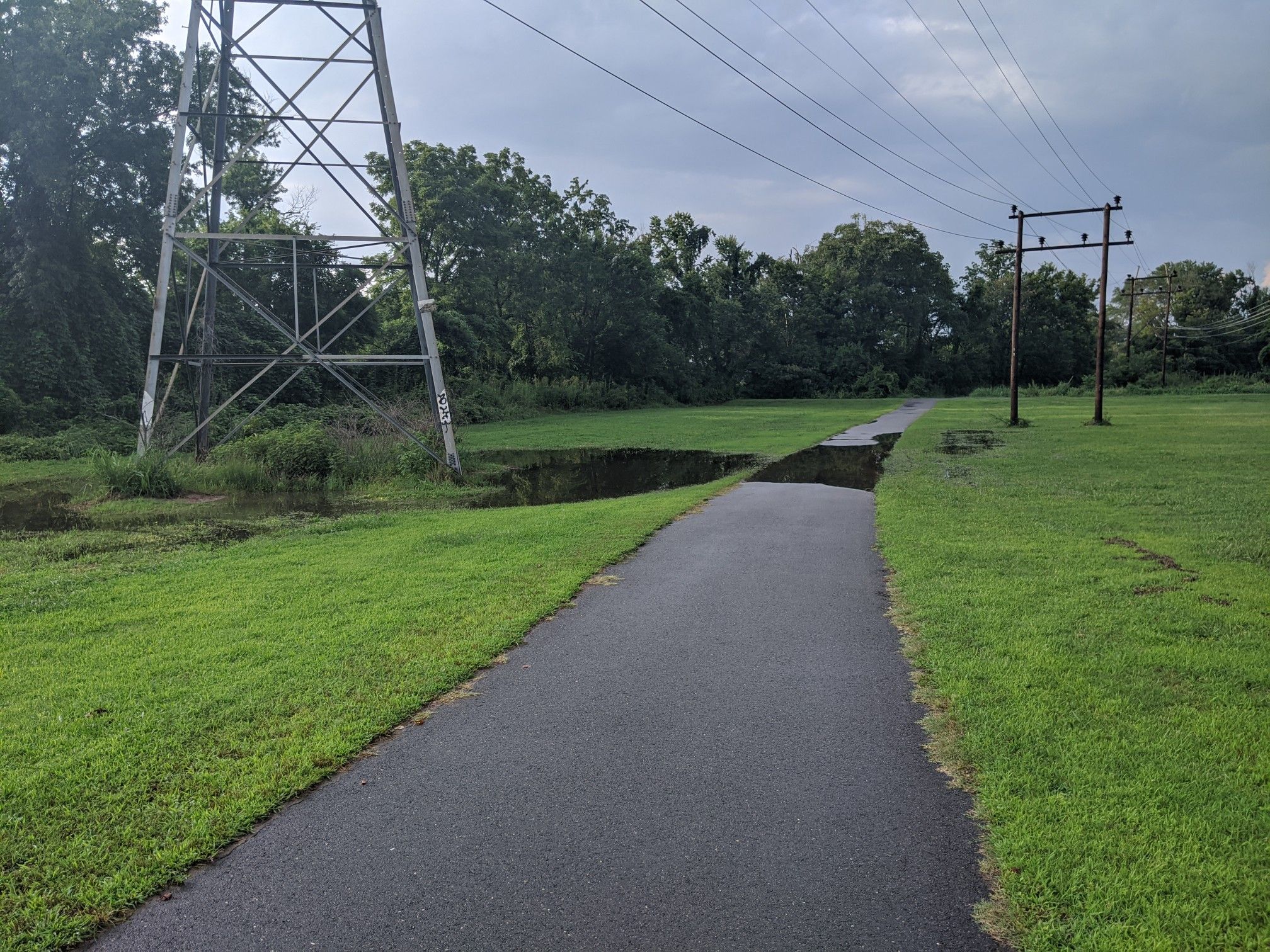 A paved path with a large gap, next to a metal power tower. - Salem Creek, Waughtown, and Peachtree Greenways Loop