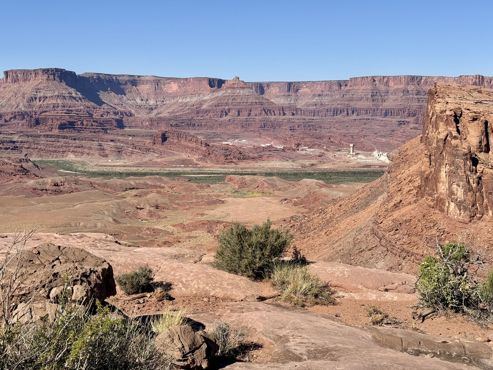 Wide view of a vast red rock canyon with a green valley below. - Captain Ahab – Best of Moab MTB Trails