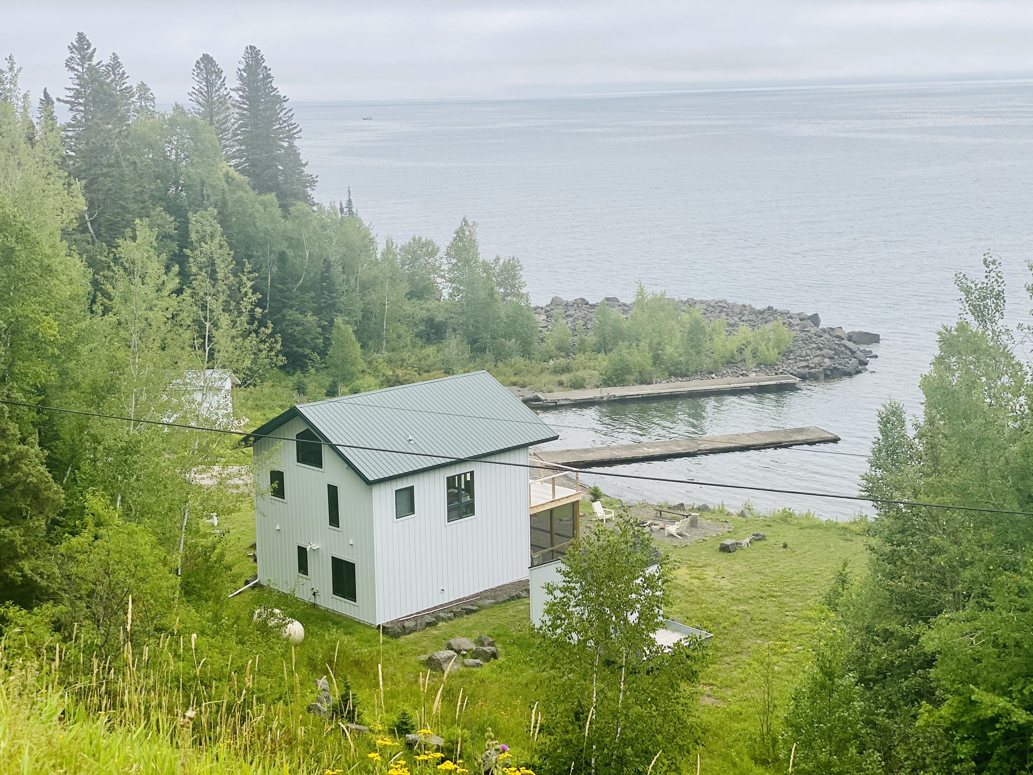 White house with a green roof by a calm lake with docks, surrounded by trees. - Cove Point Crossings loop from Split Rock Lighthouse