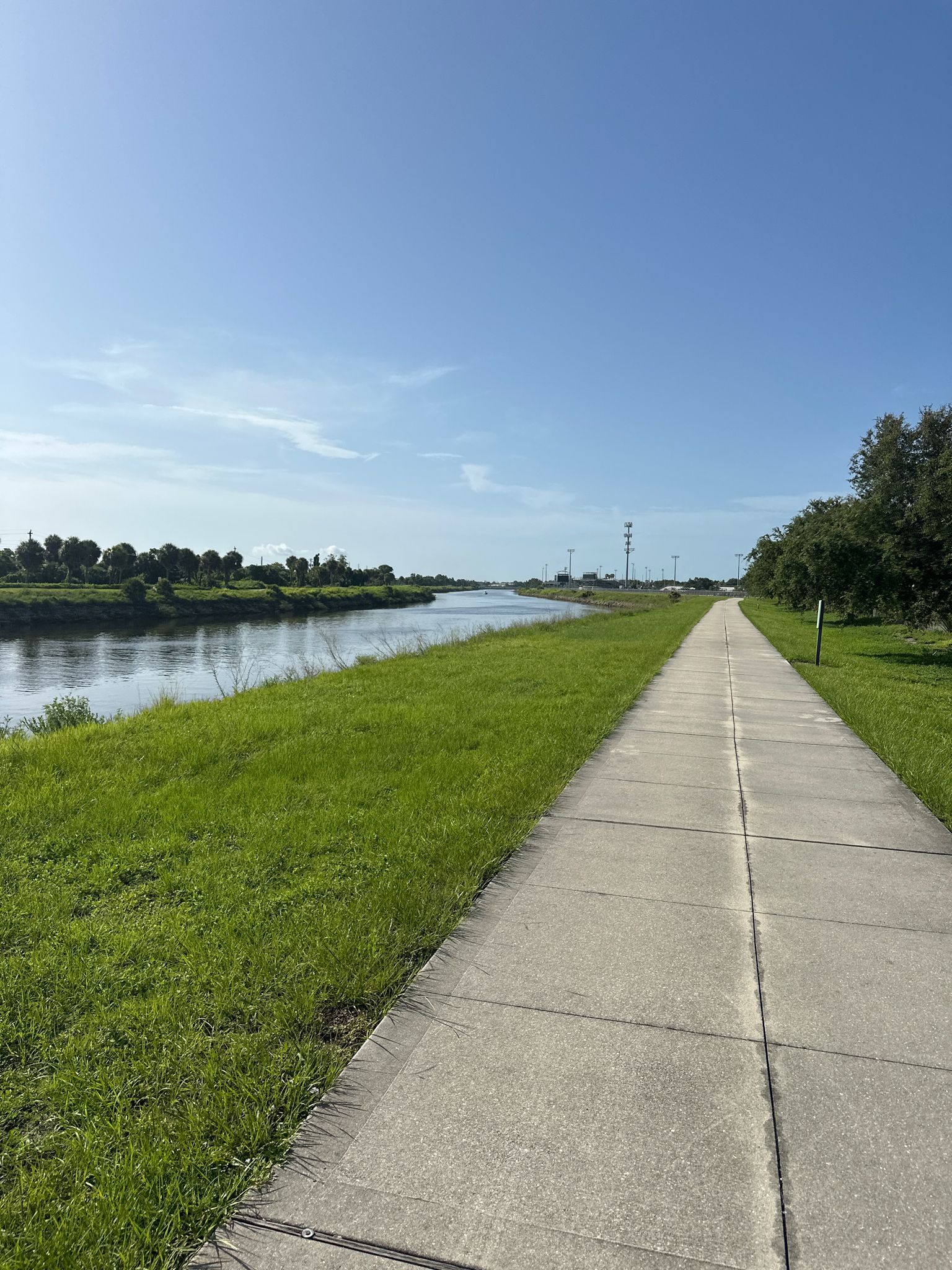 Paved path alongside a calm river with green grassy banks. - Venetian Waterway Trail