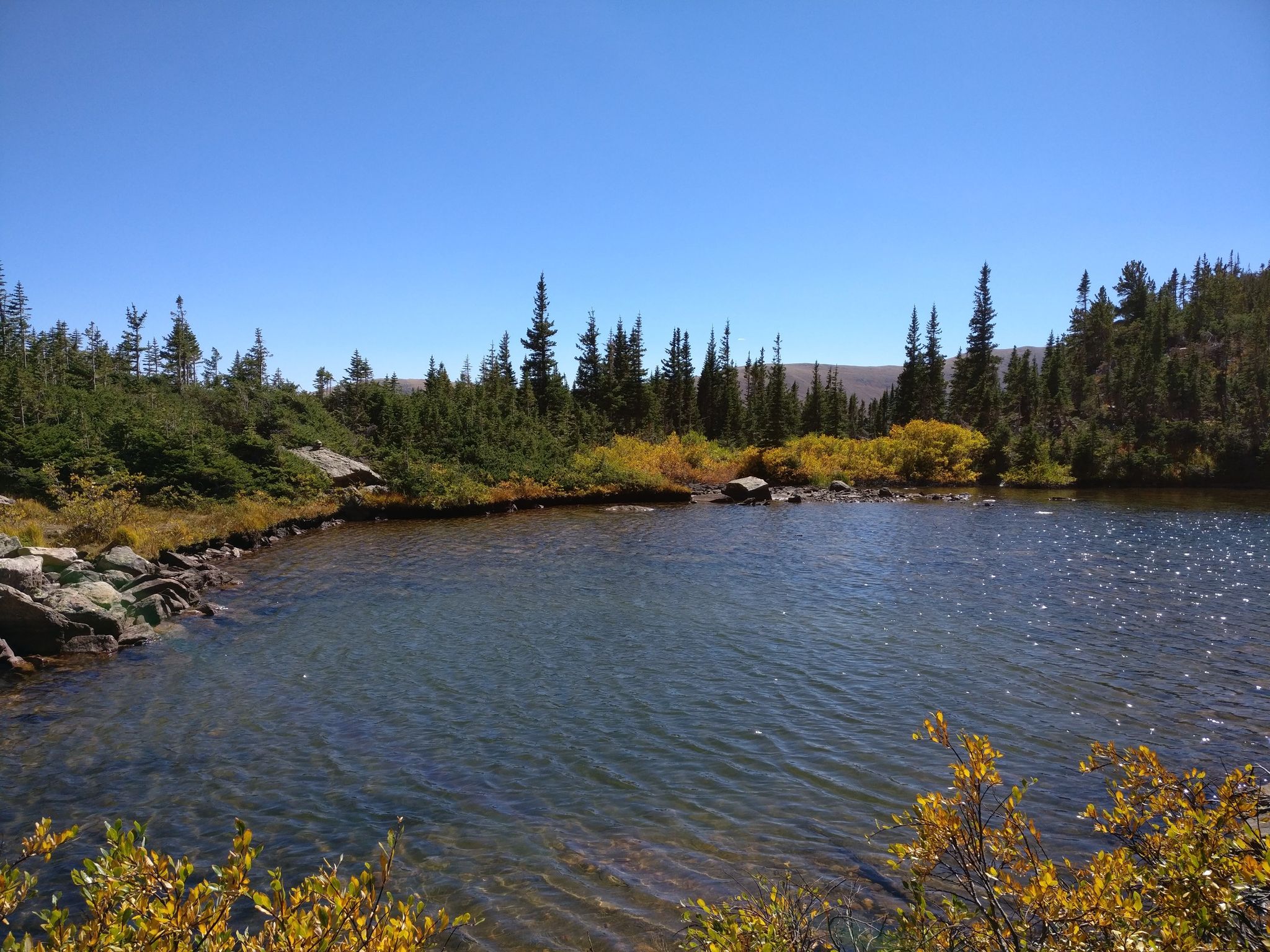 A clear mountain lake surrounded by evergreen and golden autumn trees on a sunny day. - Crater Lakes via South Boulder Creek and Crater Lakes Trail
