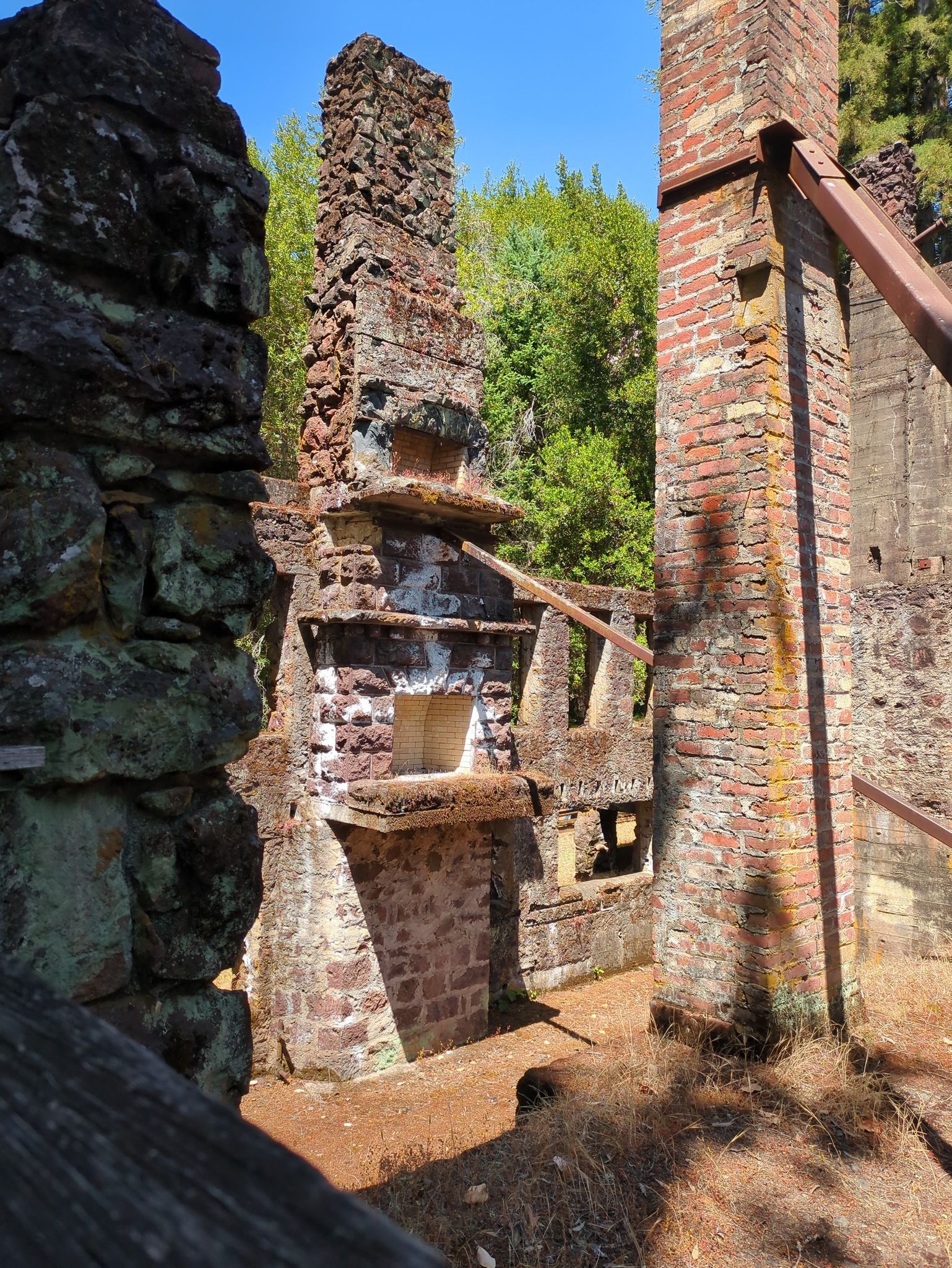 Sunny ruins of brick and stone structures amidst green trees. - Wolf House Historic Trail