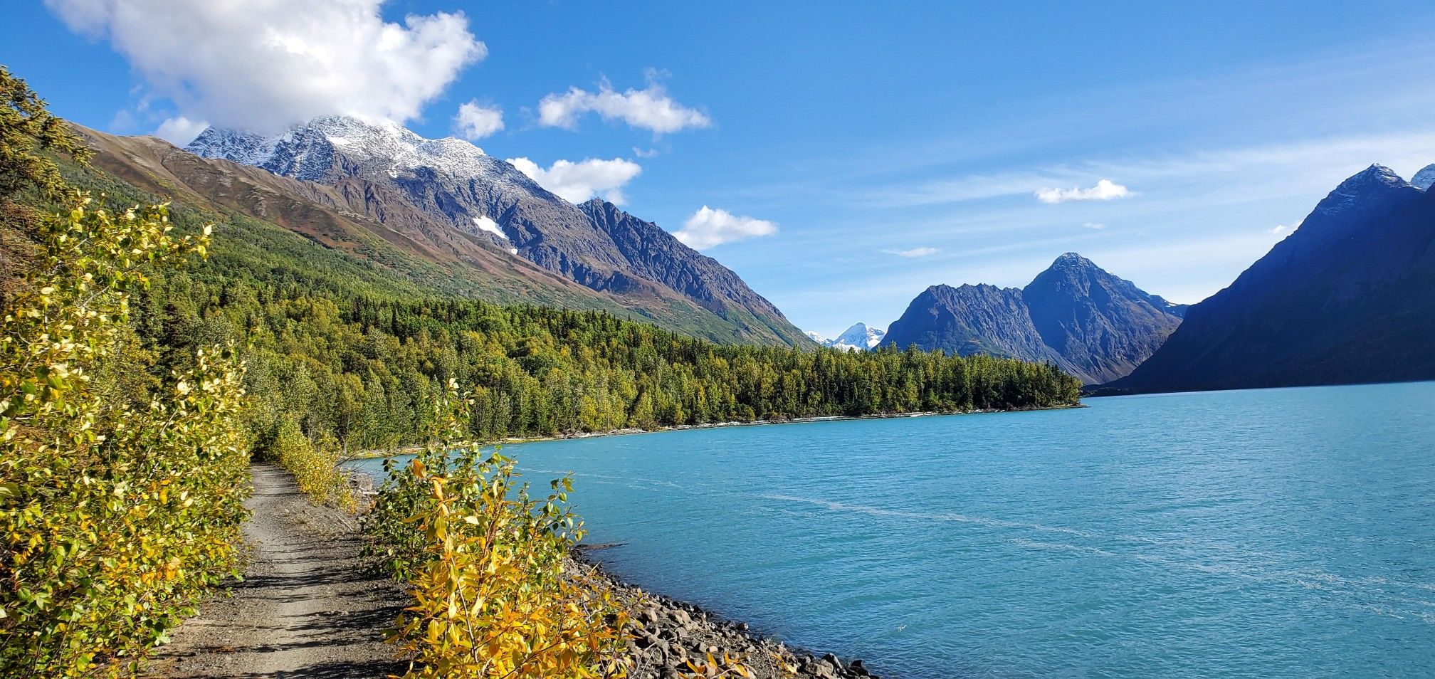 Turquoise lake, snow-capped mountains, and a gravel path on a sunny day. - Eklutna Lakeside Trail