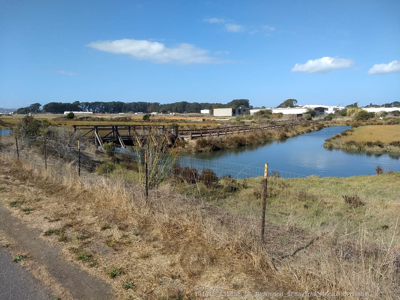 River flowing past a wooden bridge and marshland under a clear blue sky. - San Francisco Bay Trail