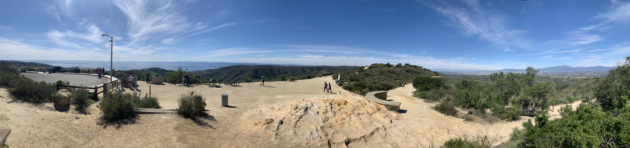 Panoramic view of a dirt lookout with distant ocean and people walking. - West Ridge and Wood Canyon Loop