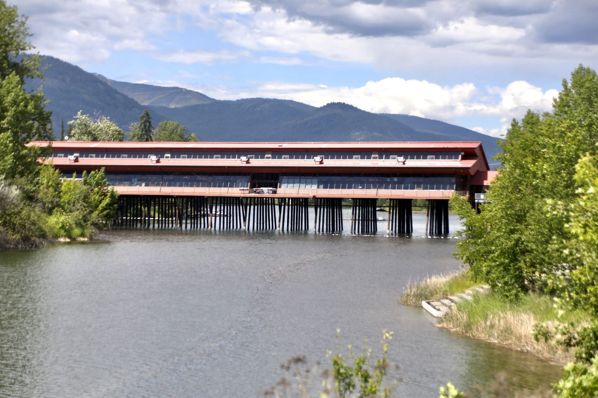 Red-roofed building on stilts over calm water, surrounded by green trees and mountains. - Running loop from Sandpoint