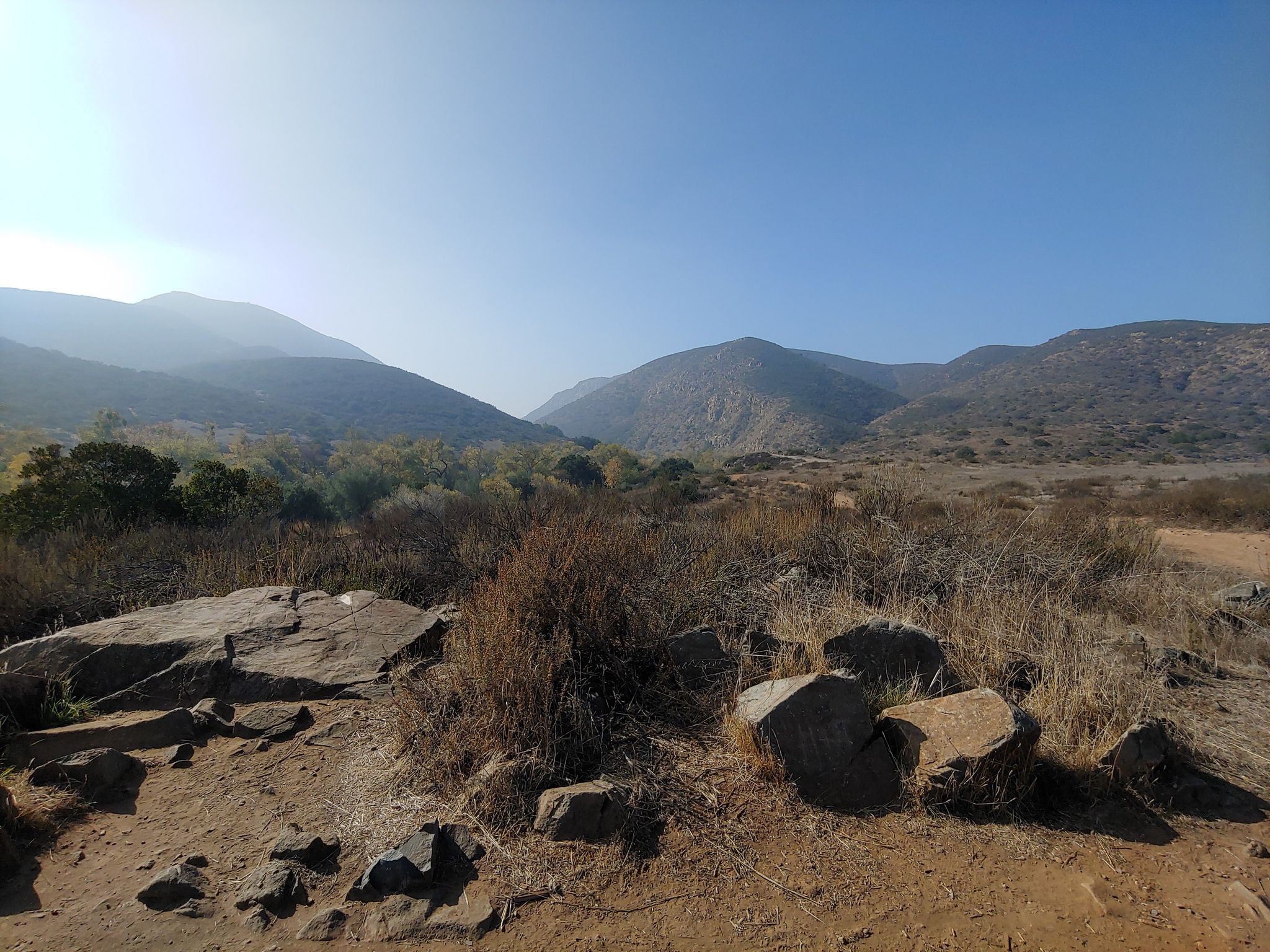 Sunny mountain valley with dry brush and distant hazy peaks. - Kumeyaay Grinding Rocks loop from Mission Gorge Rd & West Hills Pkwy
