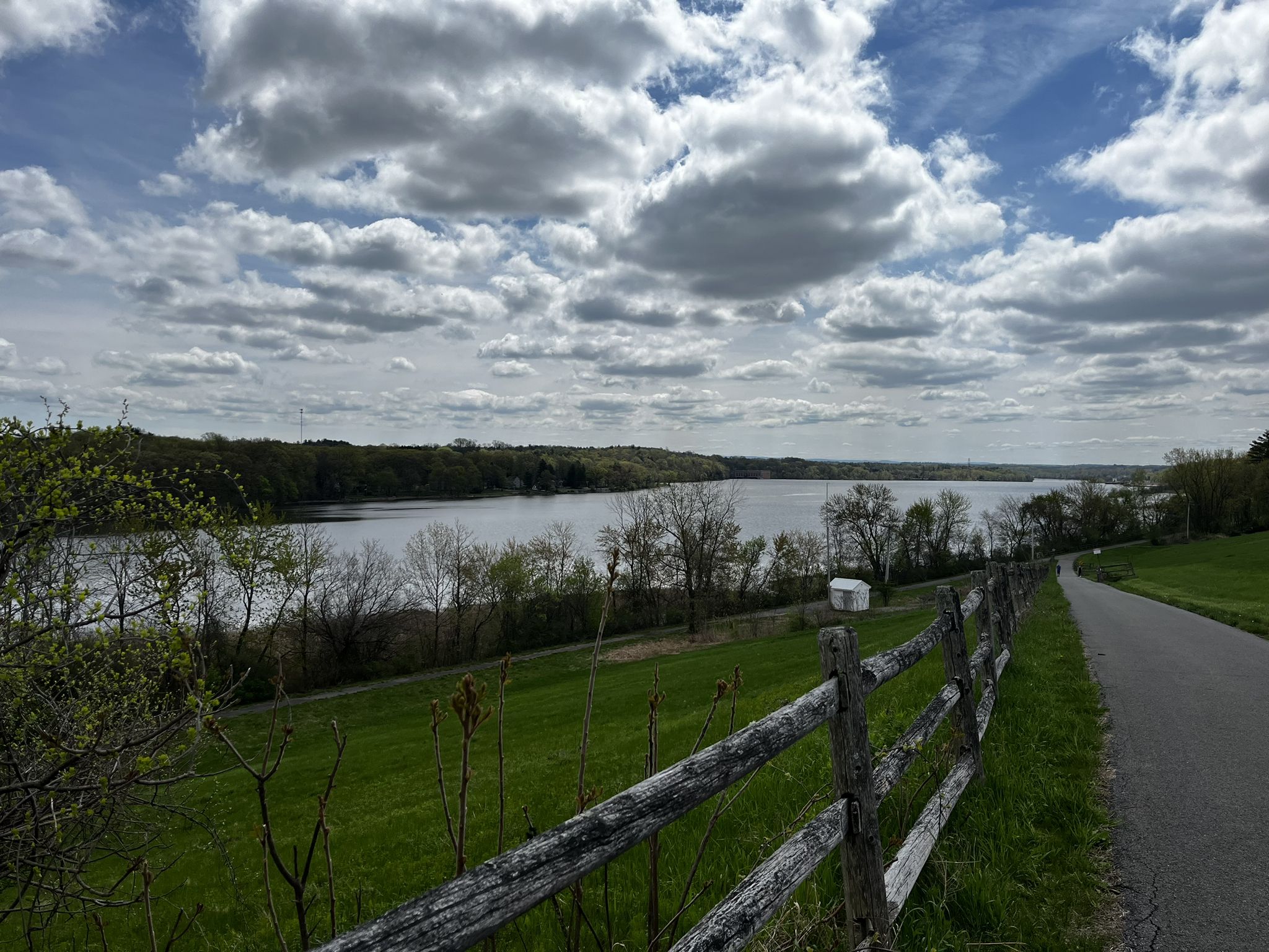 Paved path and wooden fence overlooking a wide river under a cloudy sky. - View of the Mohawk River – Mohawk-Hudson Bike & Hike Trail loop from Mohawk River State Park