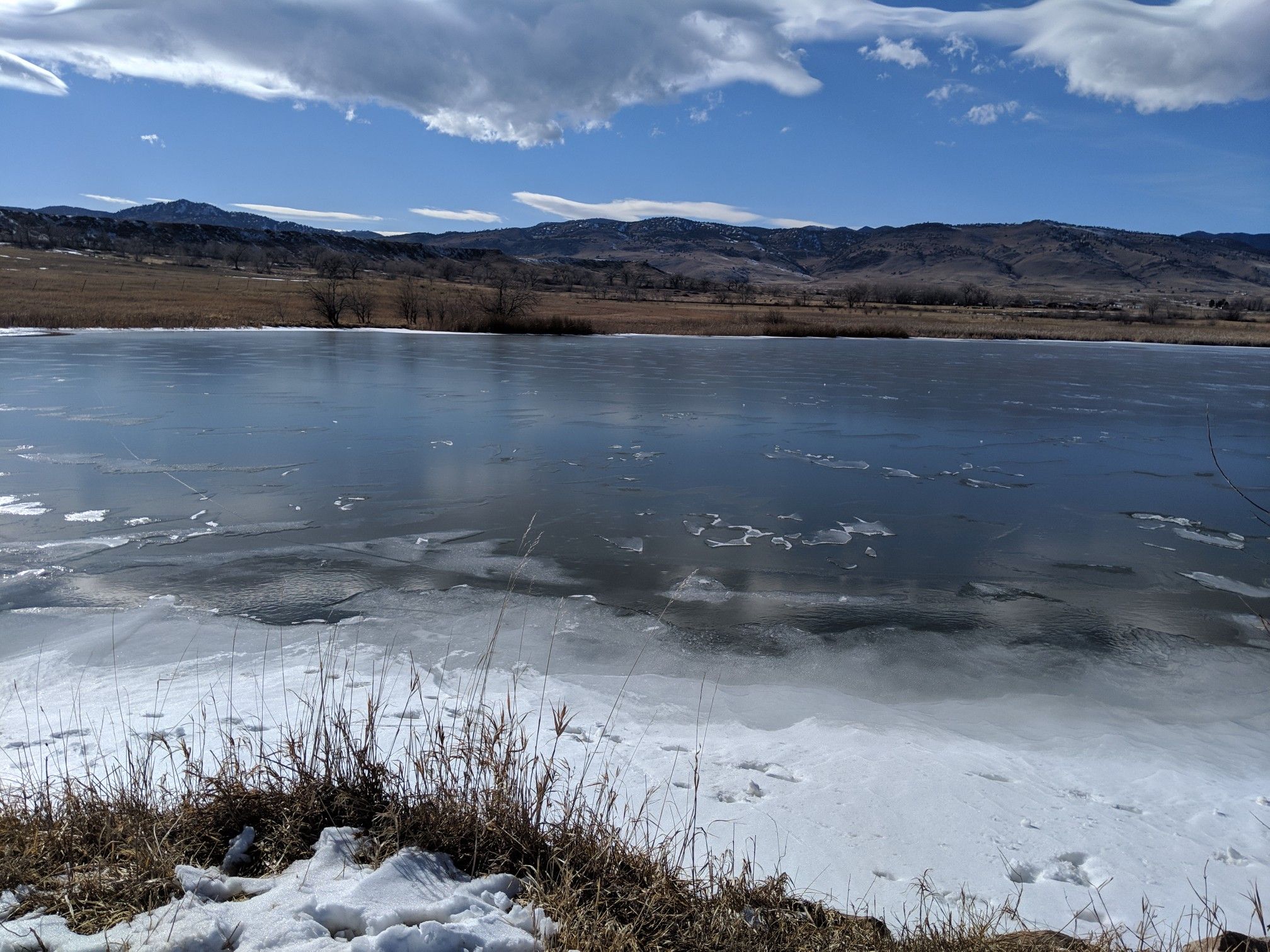 Partially frozen lake with snow-covered banks and distant mountains. - Coot Lake Dock – Boulder Valley Ranch Pond loop from Niwot