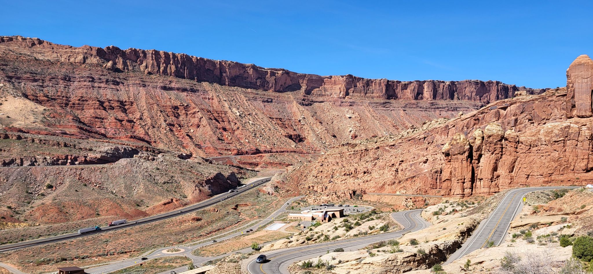 Winding roads cut through vast red rock canyons under a clear blue sky. - Courthouse Wash – Bridge over the Colorado River loop from Porcupine Rim Trailhead Parking