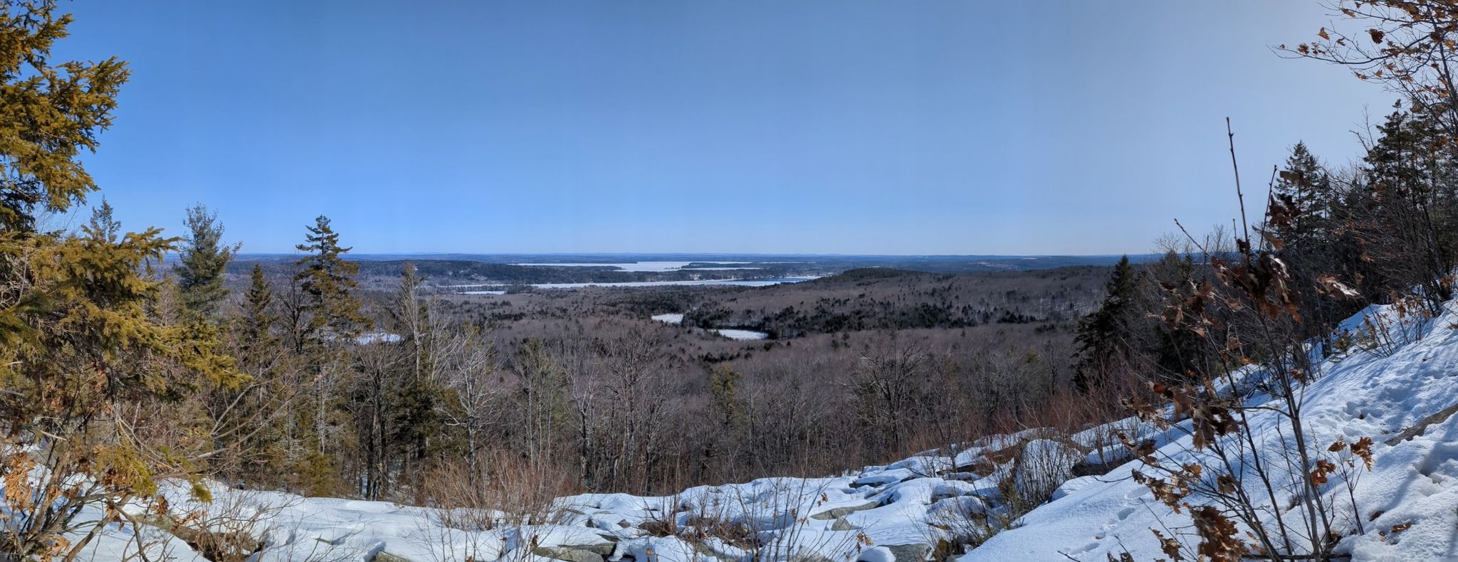 Panoramic view of a snowy forest and frozen lakes under a clear sky. - Round Top Trail