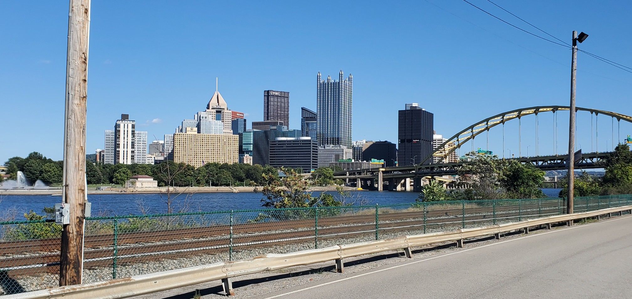 City skyline and arched bridge across a river, with railroad tracks. - Station Square Trail