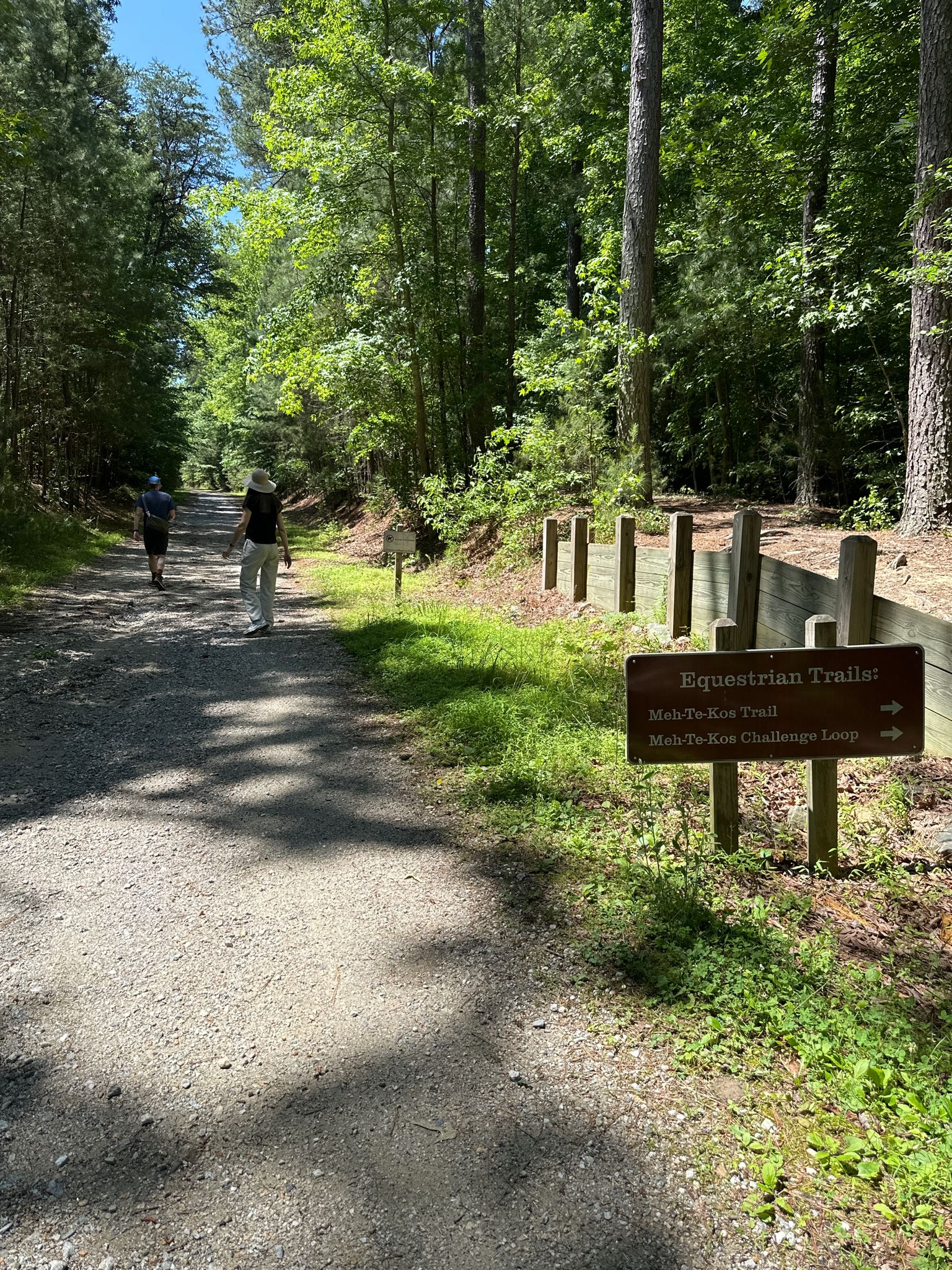 Two people walk on a sunny forest path with trail signs. - Majestic Oak and Powhatan Forks Loop via Backbone Trail