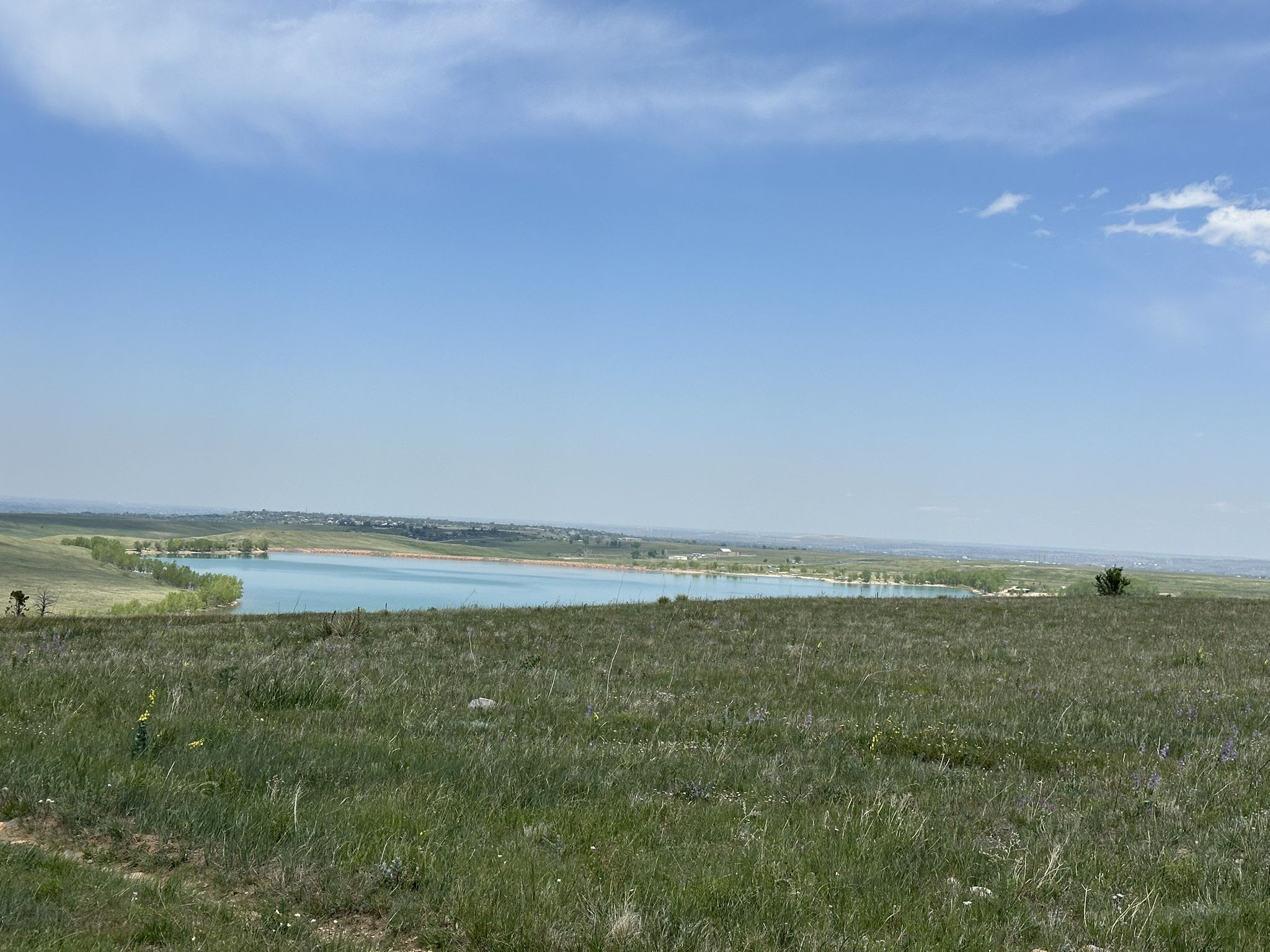 A wide view of a large lake surrounded by green and brown fields under a blue sky. - Erie to McCaslin Boulevard Climb loop