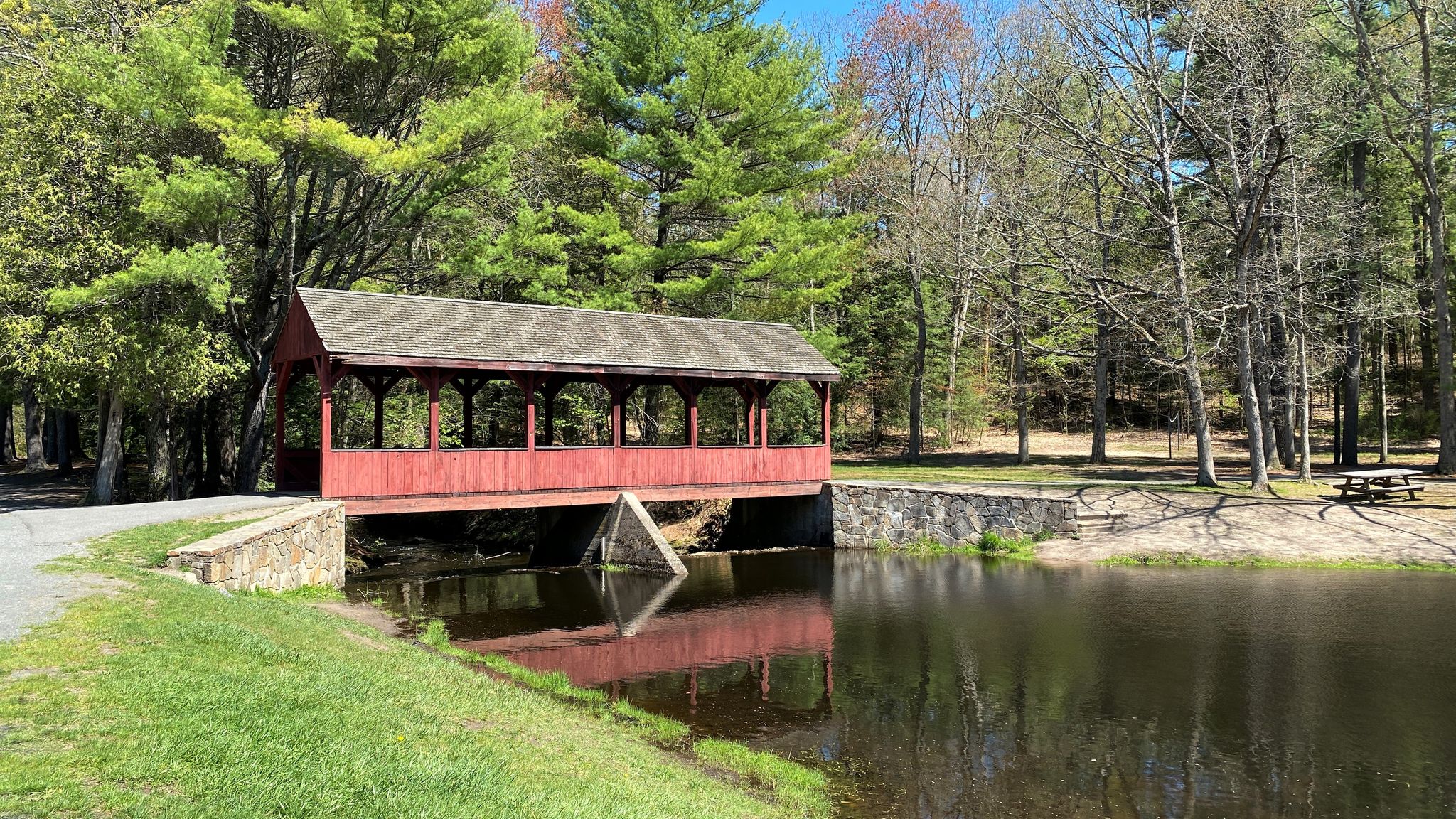 Red covered bridge over water, surrounded by green trees on a sunny day. - Running loop from Simsbury