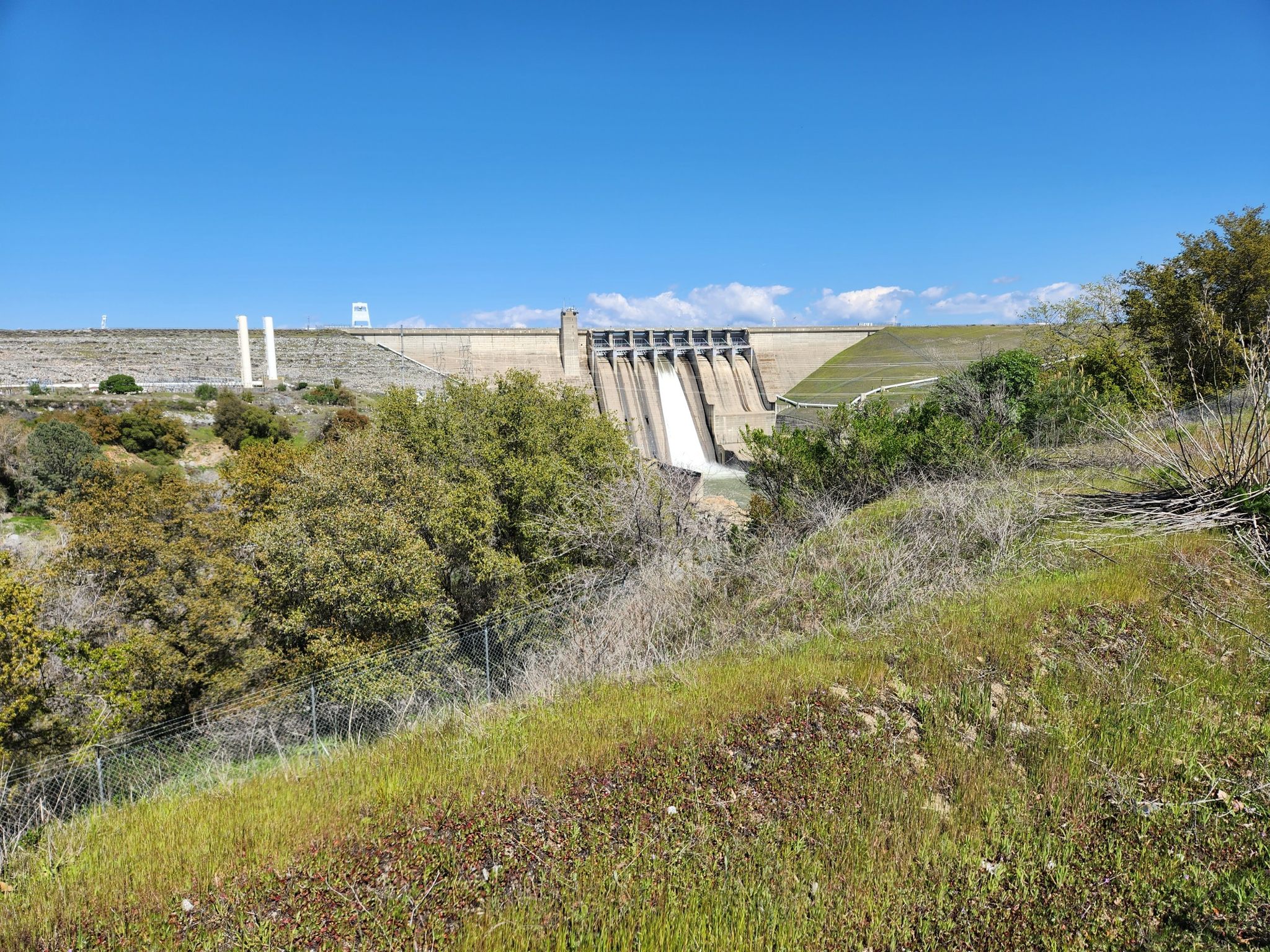 A large concrete dam with spillways visible from a grassy hillside. - Folsom Dam – Folsom Lake loop from Roseville