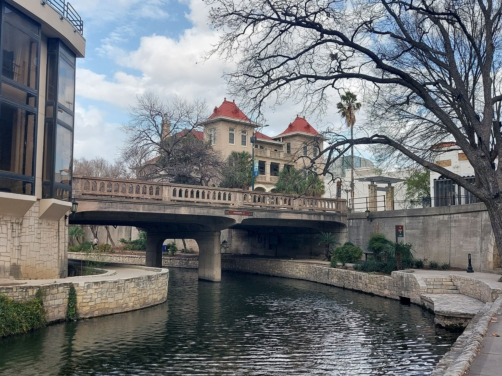 River flowing under a stone bridge with historic buildings and bare trees. - Alamo Mills Dam – River Walk loop from San Antonio