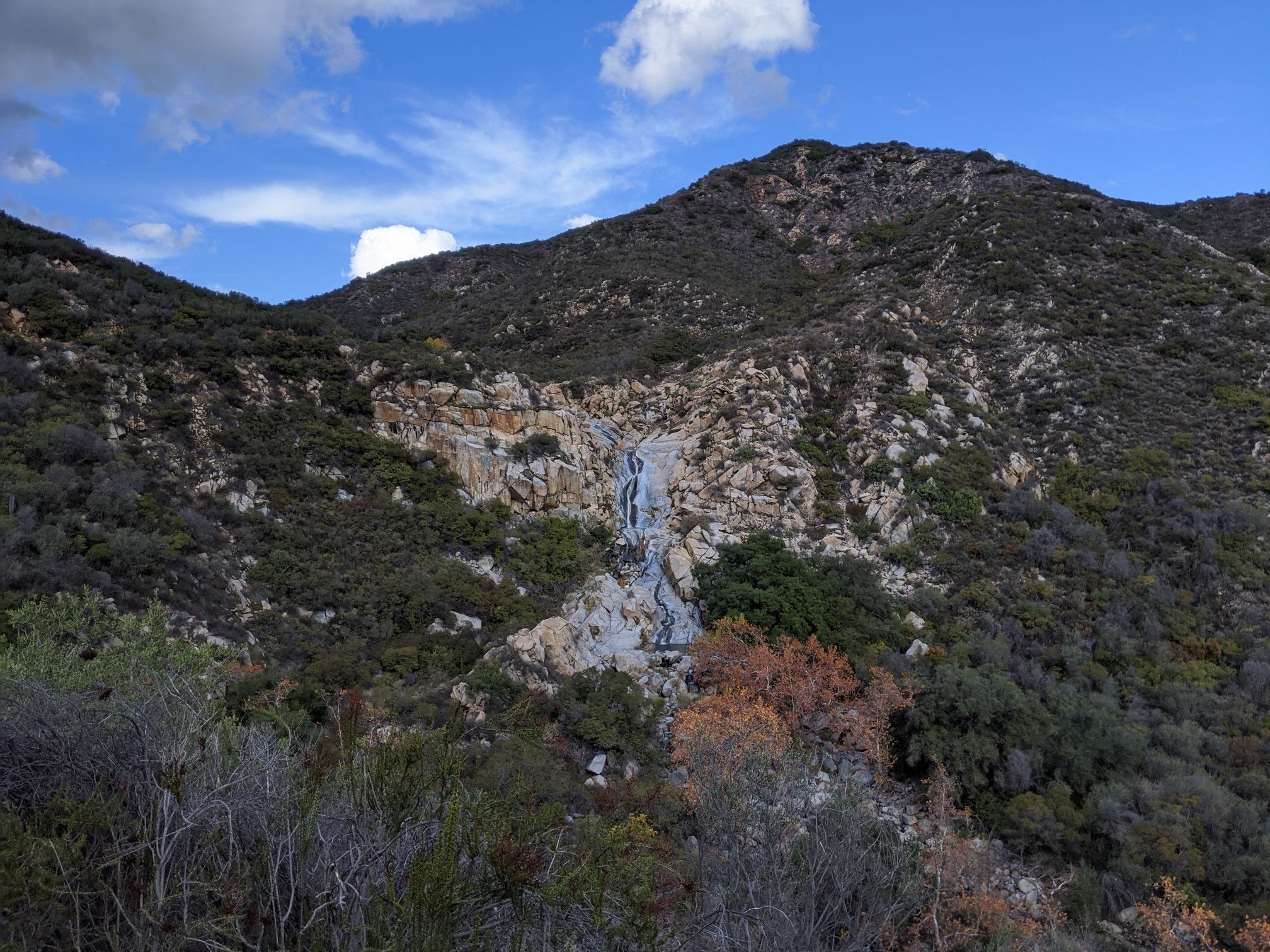 Waterfall flowing down a rocky mountain slope with green and autumn foliage. - Tenaja Falls Trail