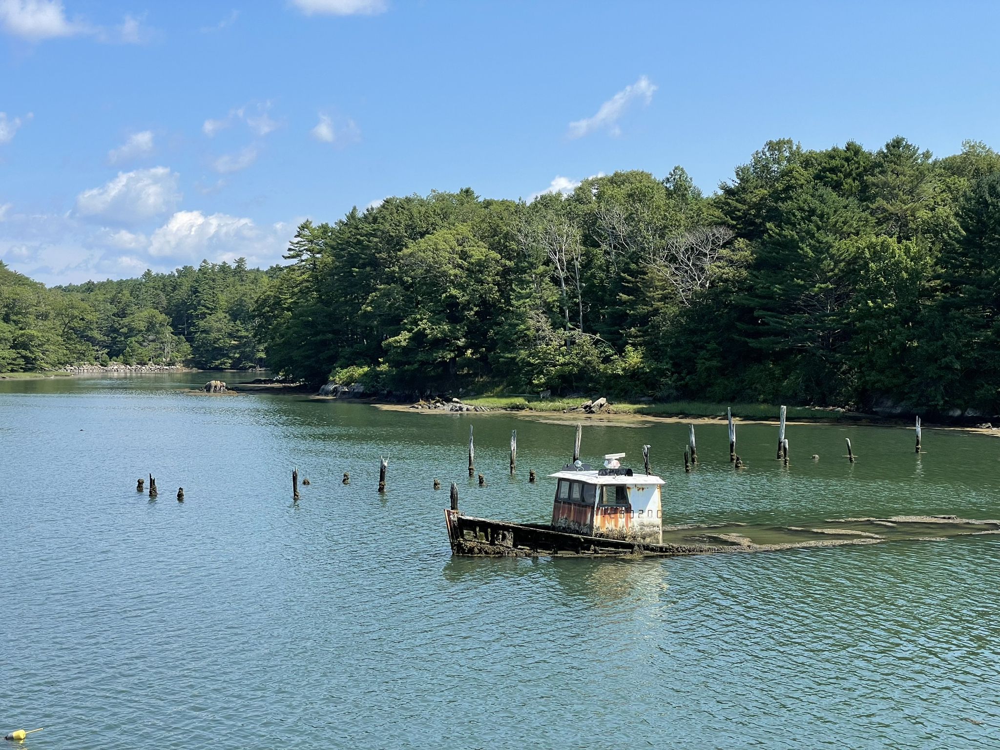 Partially sunken, rusty boat in a calm river with lush green trees. - Trevett Country Store loop from Boothbay Harbor