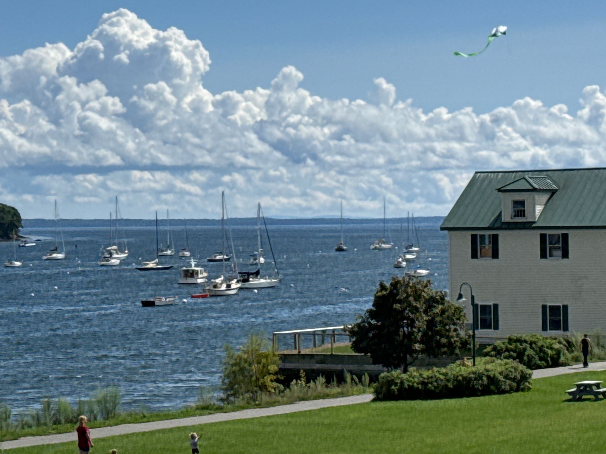 Boats on blue water, white house, green lawn, and a kite flying. - Belfast Harborwalk and Rail Trail Loop