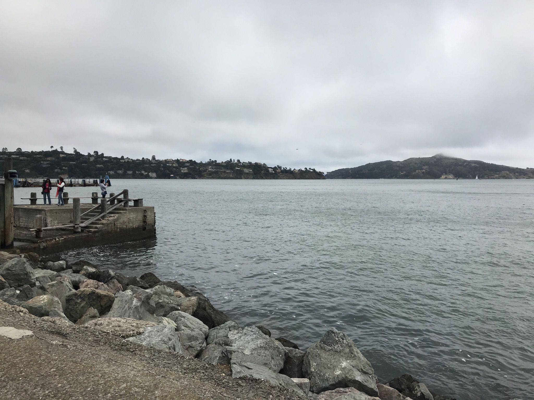 People on a wooden pier over calm water, rocky shore, overcast sky. - Downtown Sausalito – Sausalito Waterfront loop from Sausalito