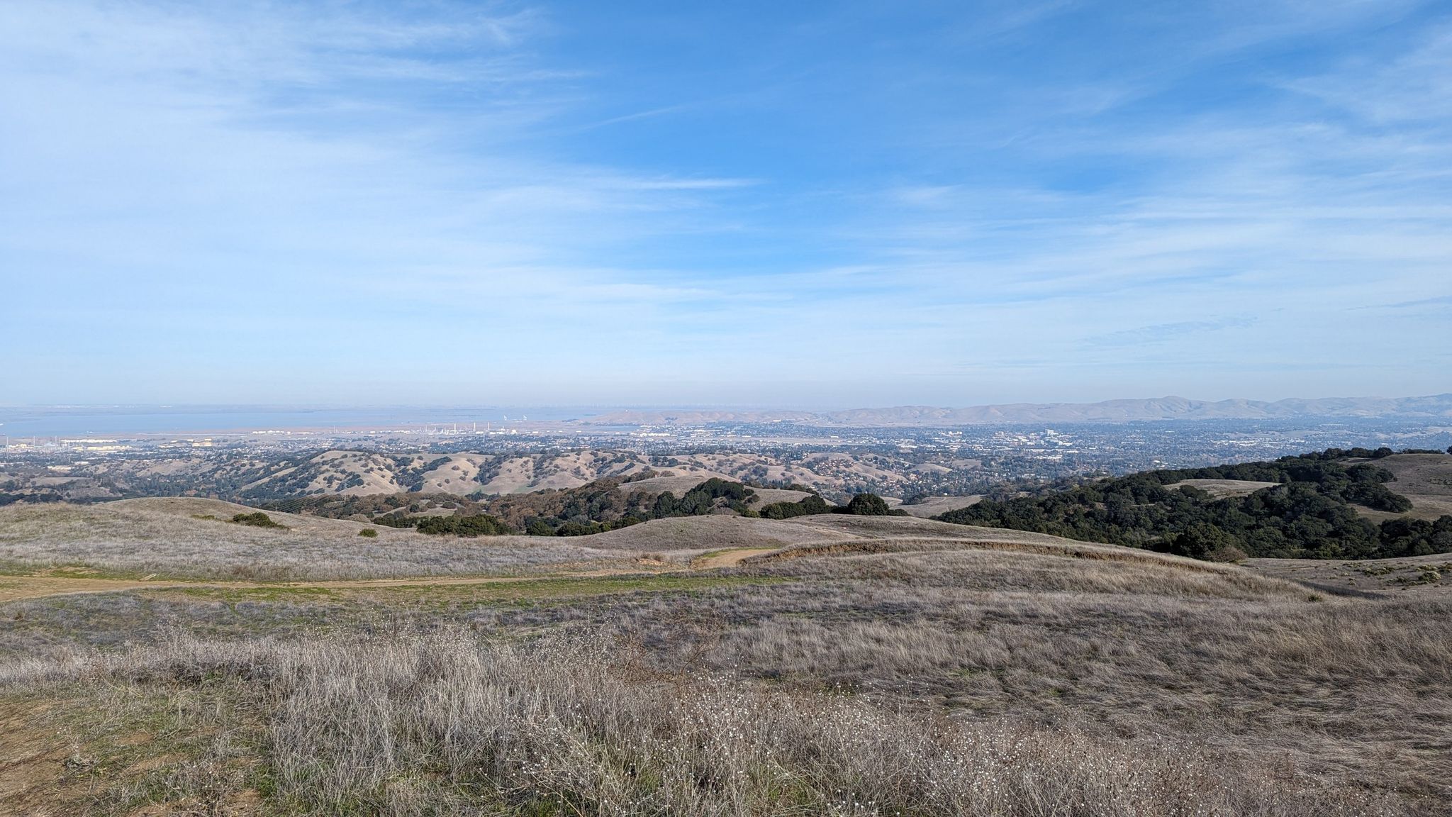 Expansive view of dry, rolling hills overlooking a distant city under a bright sky. - Abrigo Valley and Mott Peak Loop