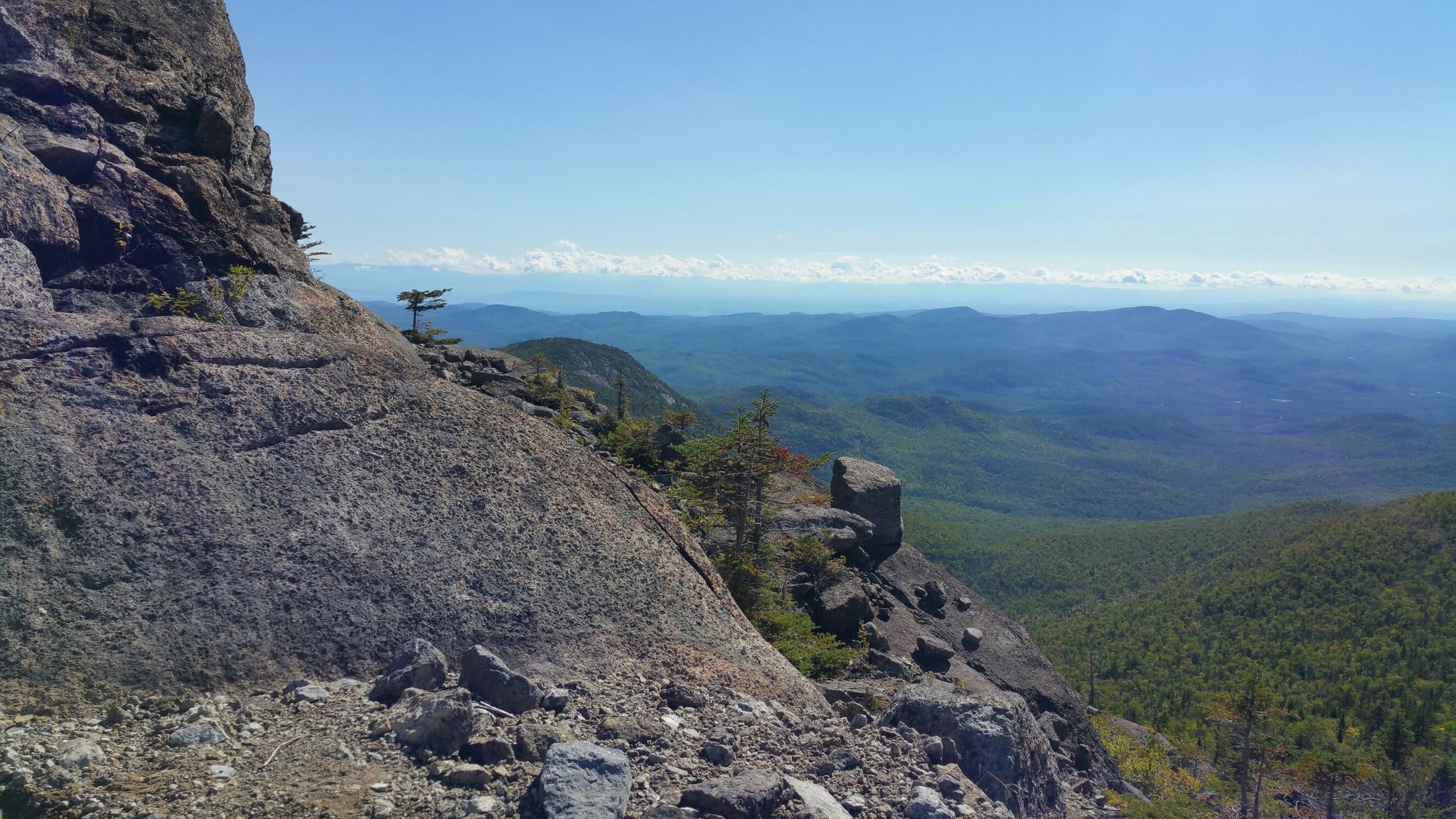 Steep rocky cliff overlooking vast forested mountains under a clear blue sky. - Dix Range Traverse