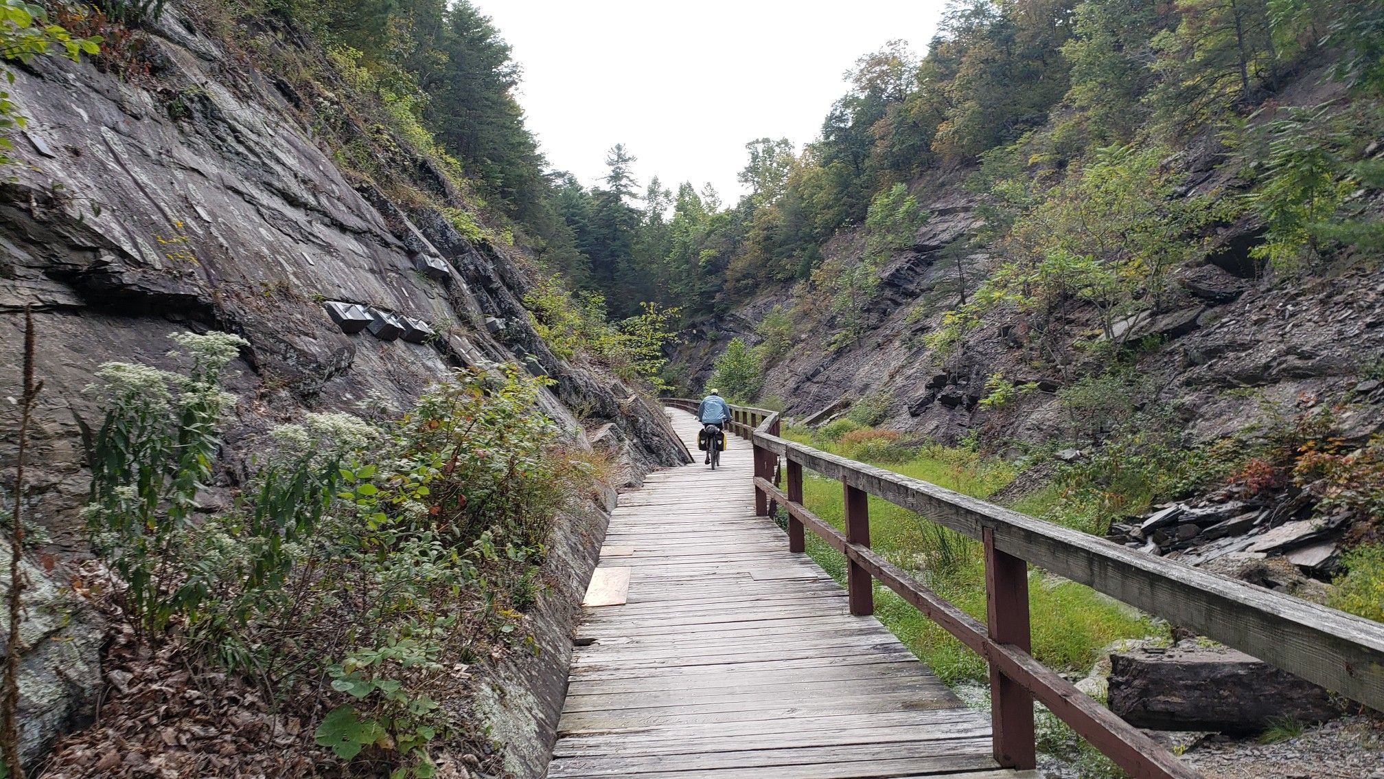 Person cycling on a wooden boardwalk through a narrow, rocky gorge. - Green Ridge State Forest – View of the Potomac River loop from Little Orleans