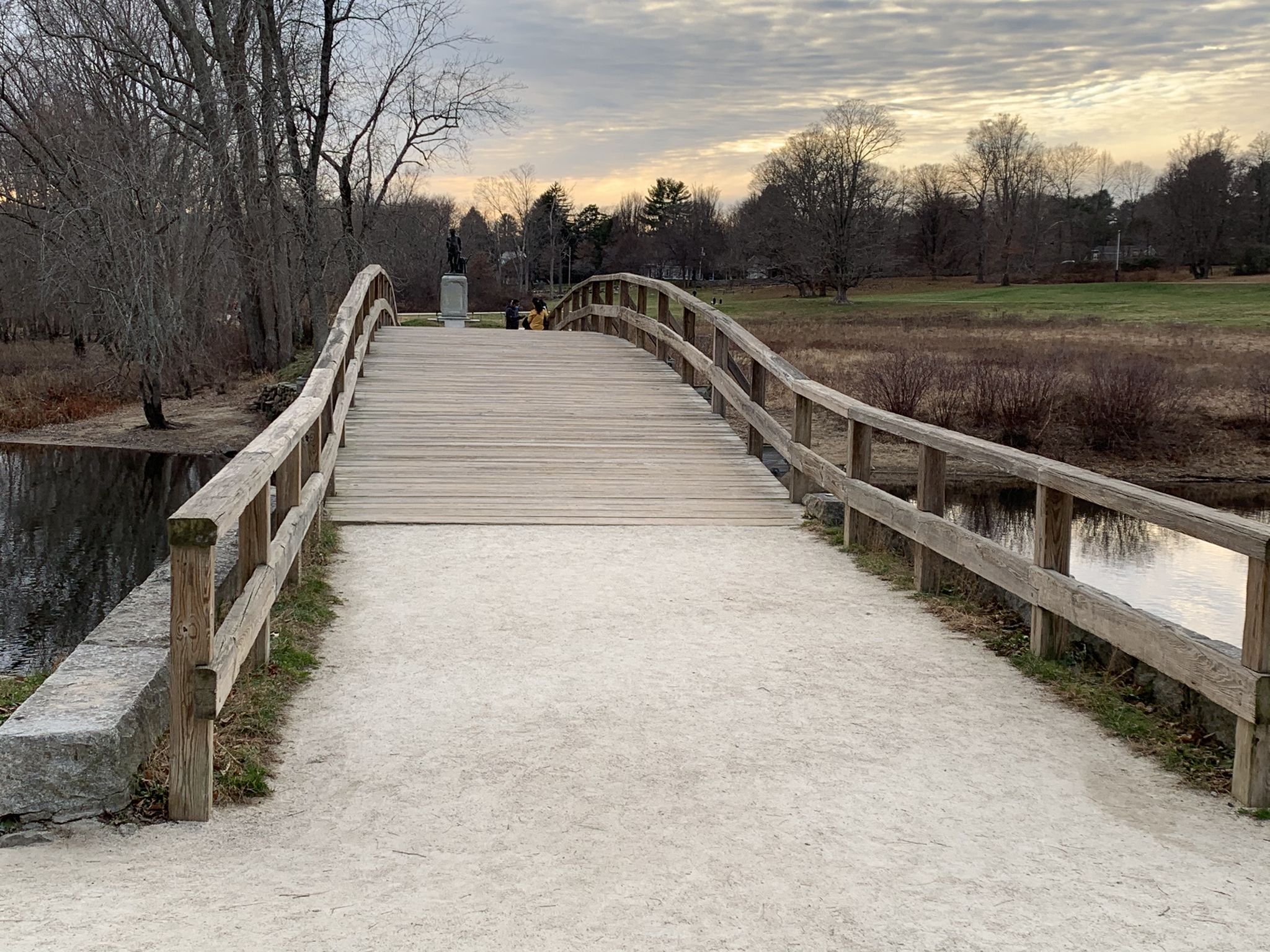 A wide wooden pedestrian bridge crosses calm water under an overcast sky. - Old North Bridge – Concord Monument Square loop from Page Brook Reservation