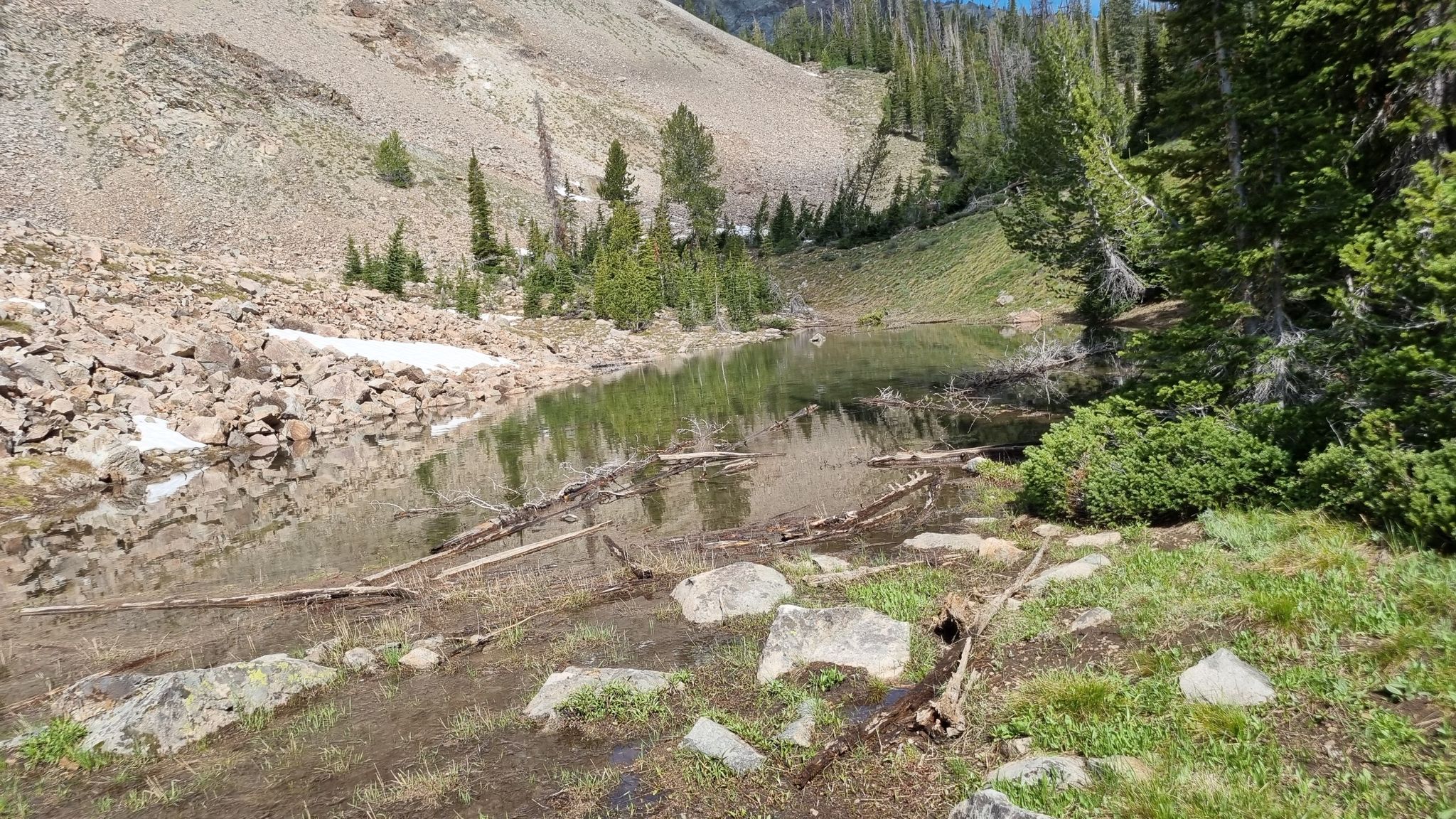 Sunny alpine lake with rocky shores, snow patches, and evergreen trees. - Norton Lakes and Prairie Lakes Loop Trail