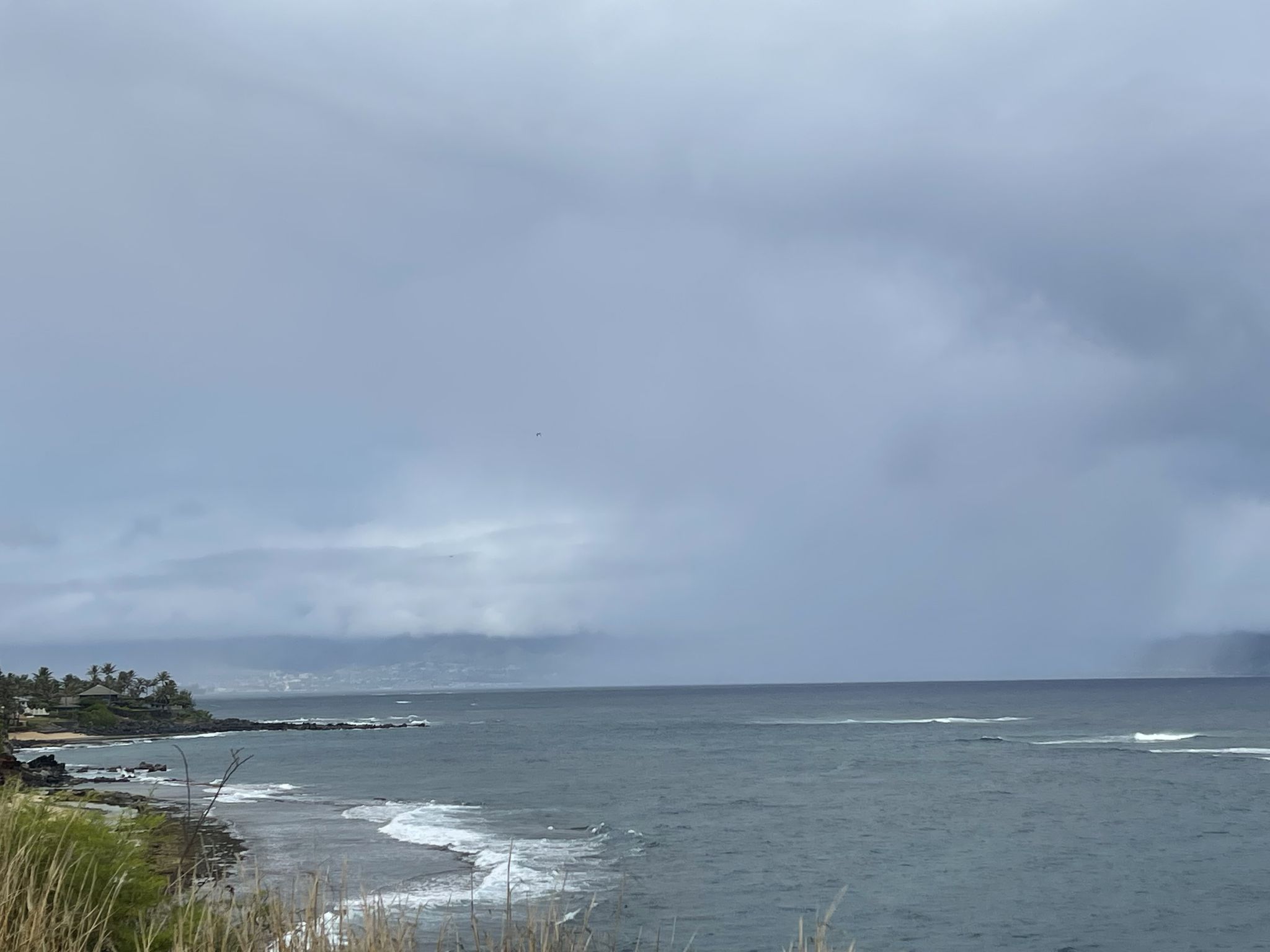 Overcast sky above a dark ocean with waves crashing on a rocky coastline. - North Pāʻia Beach – Rodeo General Store loop from Kauhikoa