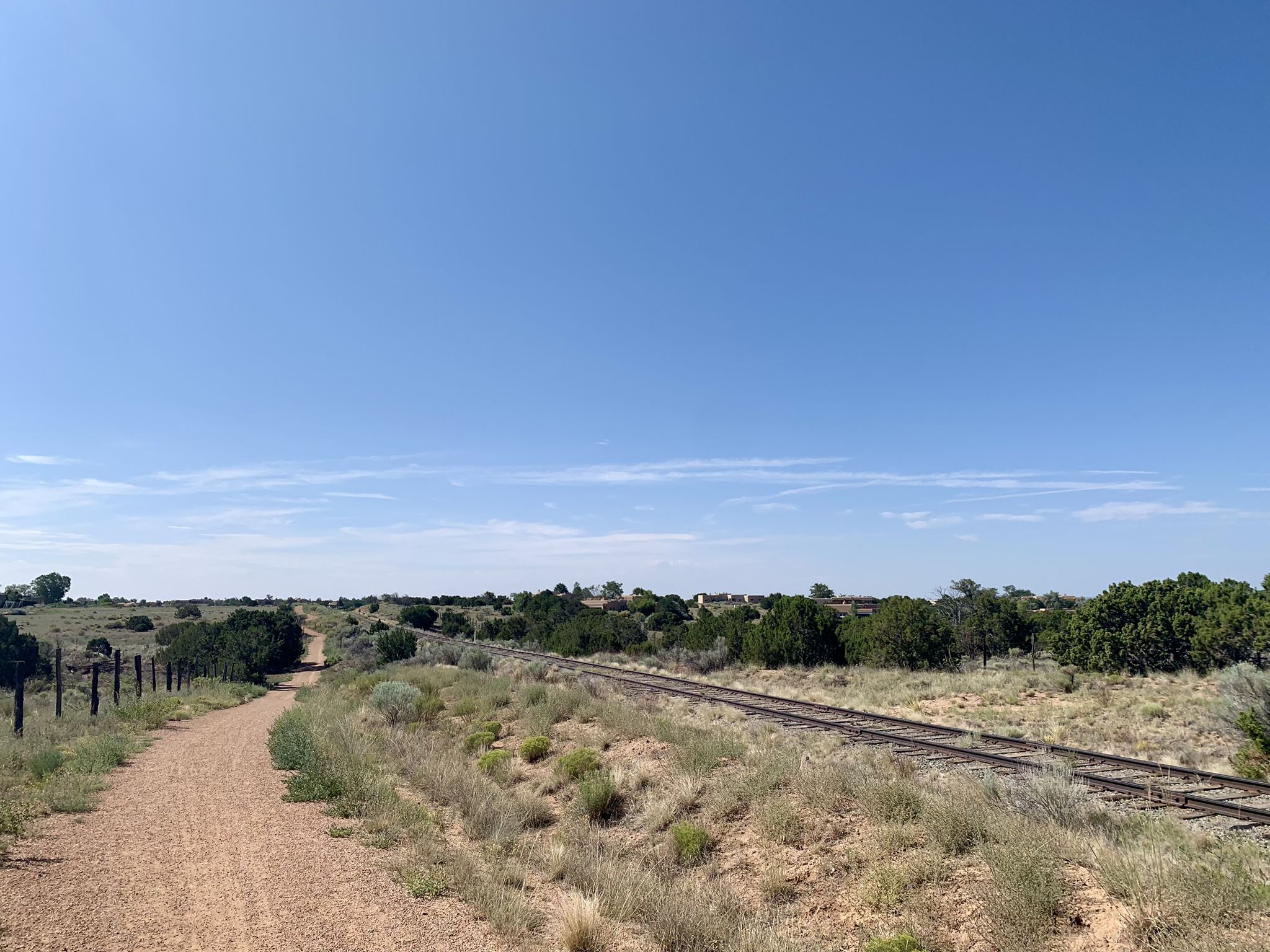 A dirt path runs alongside train tracks through a sunny, arid landscape. - Santa Fe Rail Trail