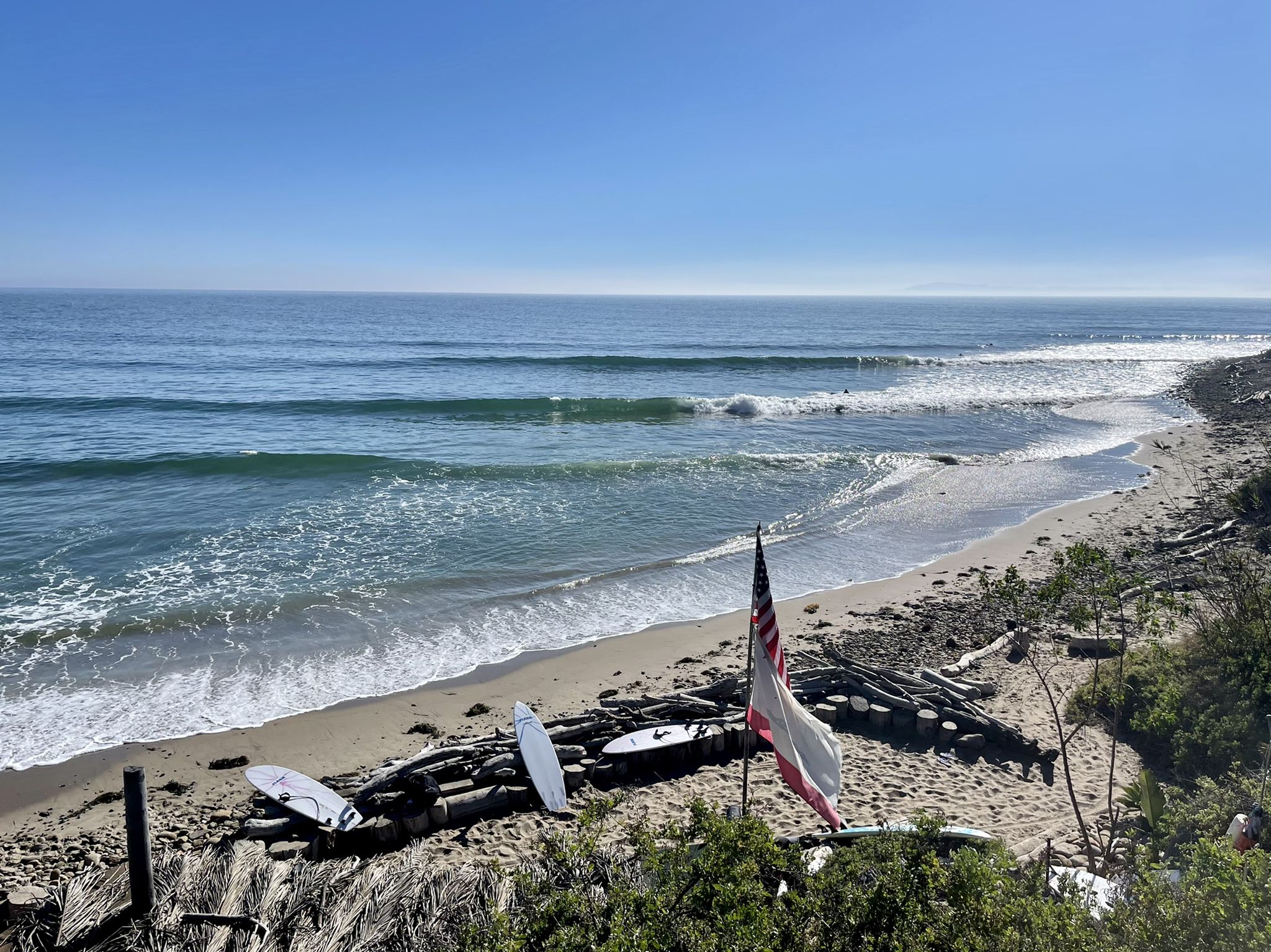 Sunny beach with waves, surfboards, and an American flag on sand. - Lake Casitas Loop