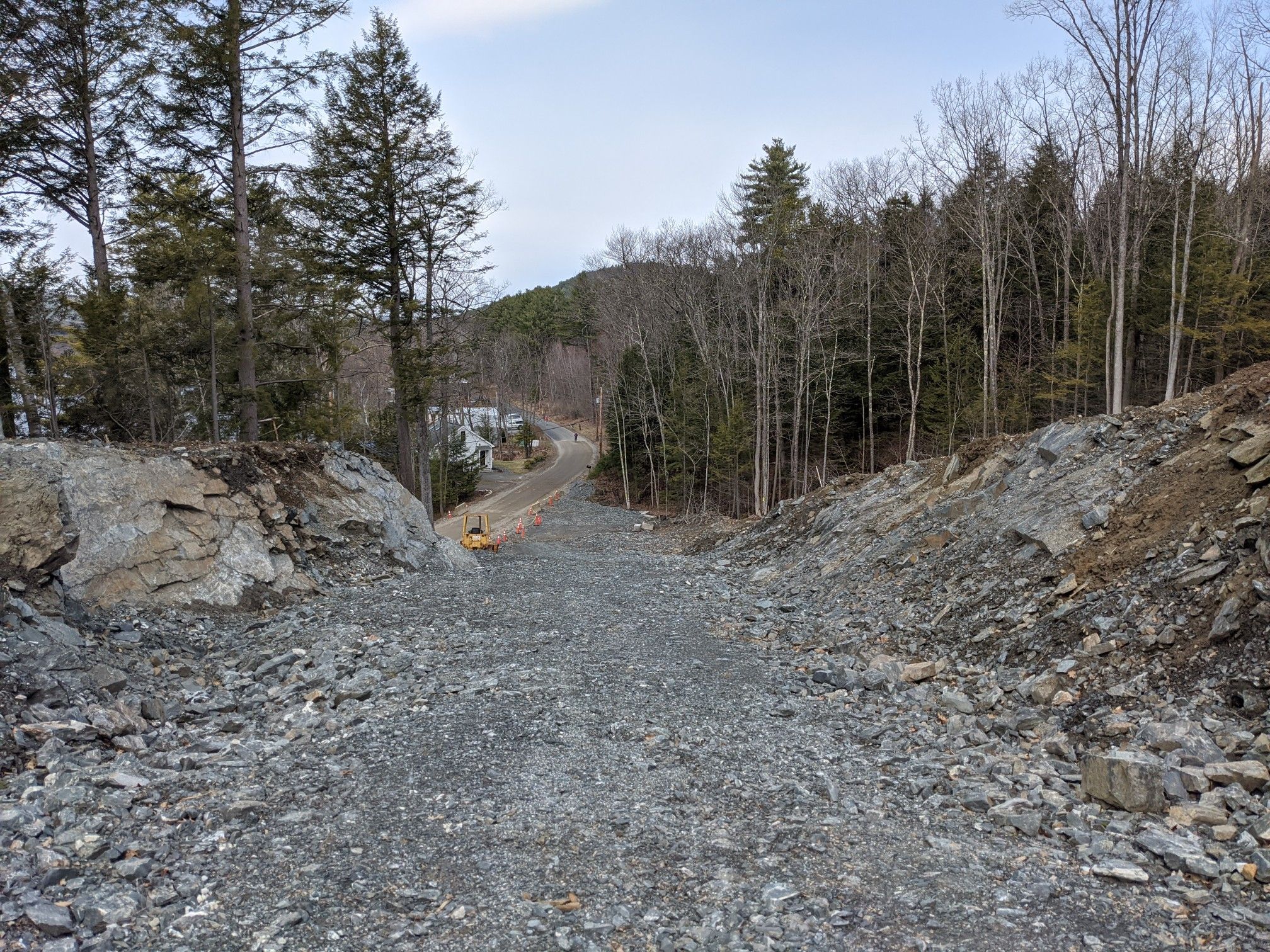 Rocky path descending towards a paved road through a forested landscape under cloudy skies. - Connecticut River – Lyme Road loop from Ferguson Field