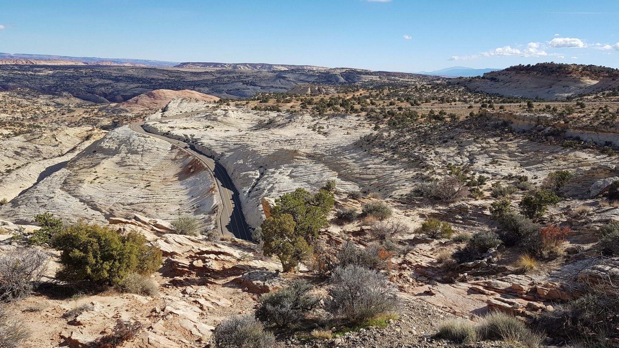 Arid landscape with light-colored rock formations and a dry wash under blue sky. - Boulder to Escalante Cycle Route