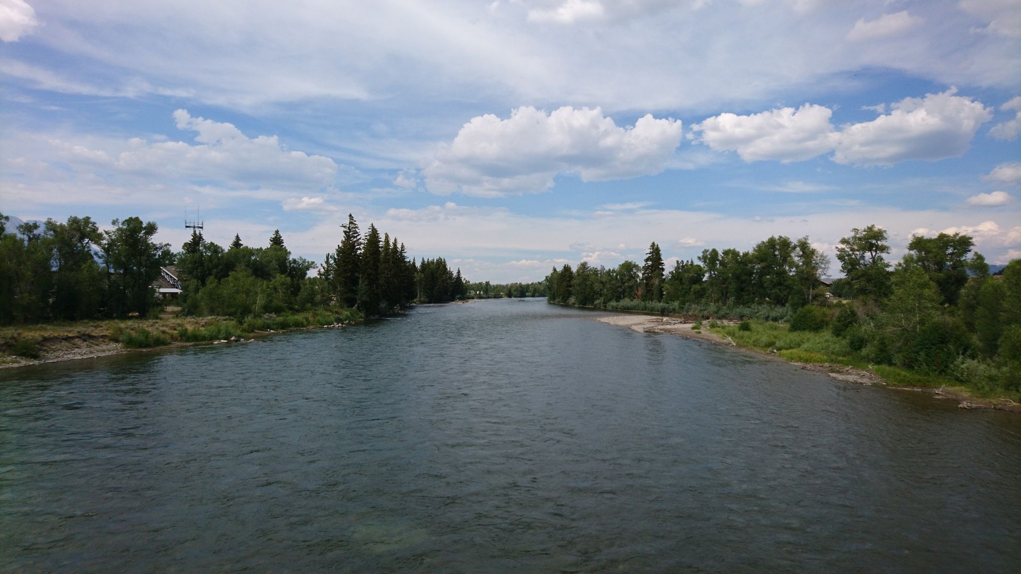 Wide river with green trees on banks under a cloudy blue sky. - Moose Junction – Moose Wilson Pathway loop from Murie Ranch Historic District