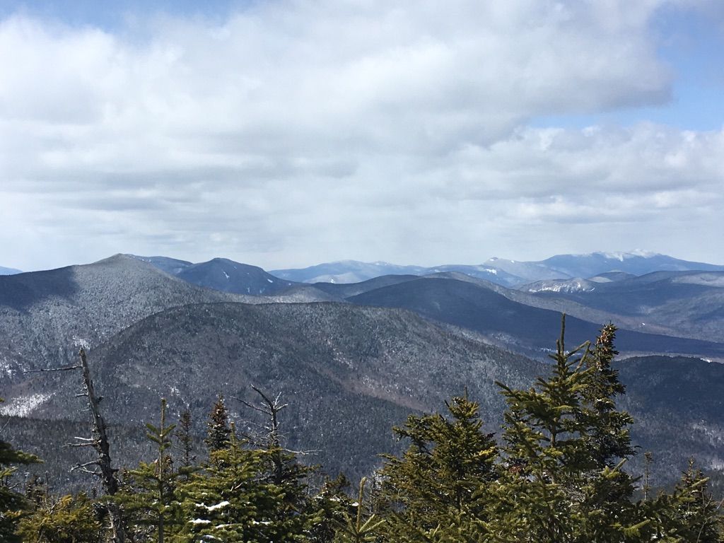 Snow-dusted mountain range under a bright, cloudy sky with evergreen trees. - Mount Whiteface and Passaconaway Loop