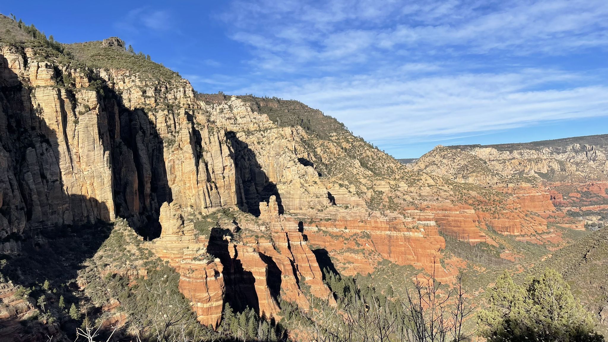 Layered rock canyon with red and tan cliffs under a bright blue sky. - North Wilson Mountain Trail