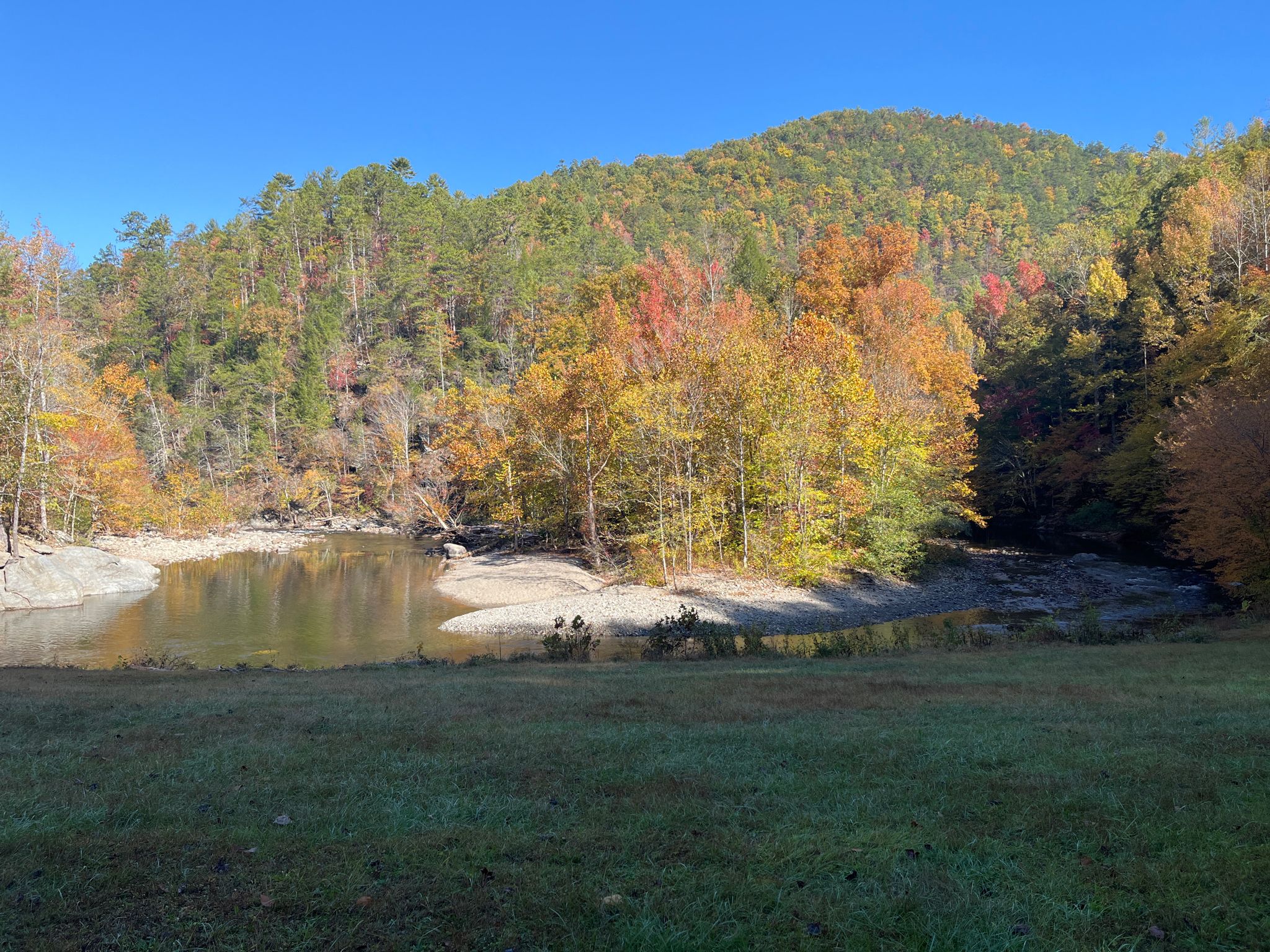 Calm river reflecting vibrant autumn trees and a distant green mountain. - Cades Cove Loop Road – Beautiful view of the Valley loop from Townsend