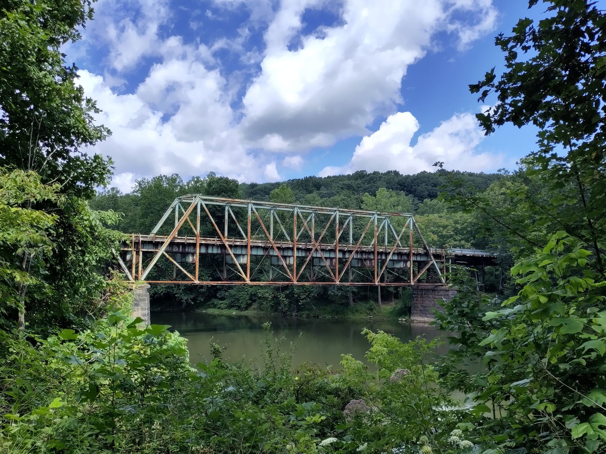 An old metal truss bridge spans a river under a cloudy sky. - Great Allegheny Passage: Layton to Dawson