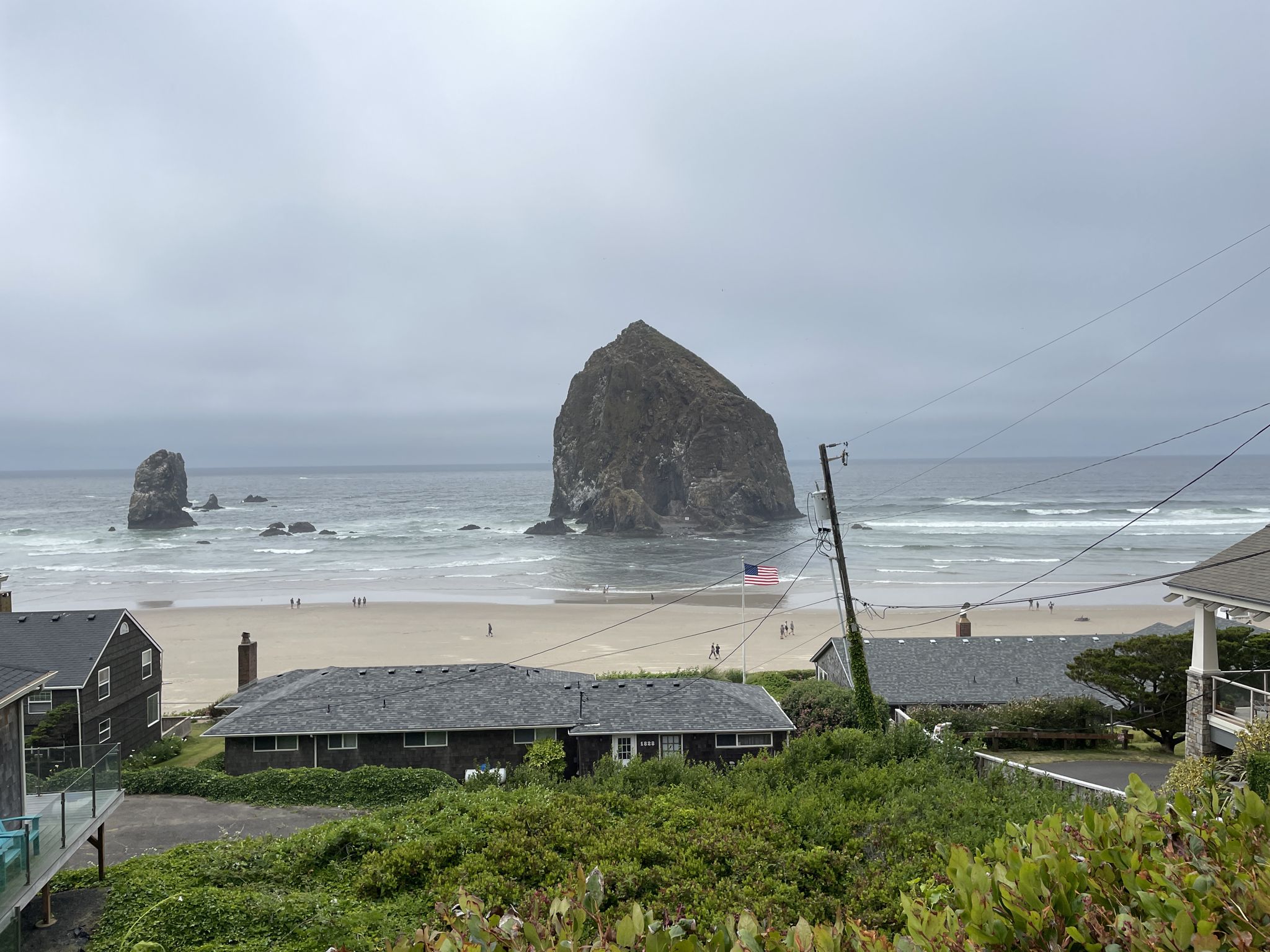 Overcast view of a large sea stack, ocean, beach, and coastal houses. - Haystack Rock & Elk Creek Road loop