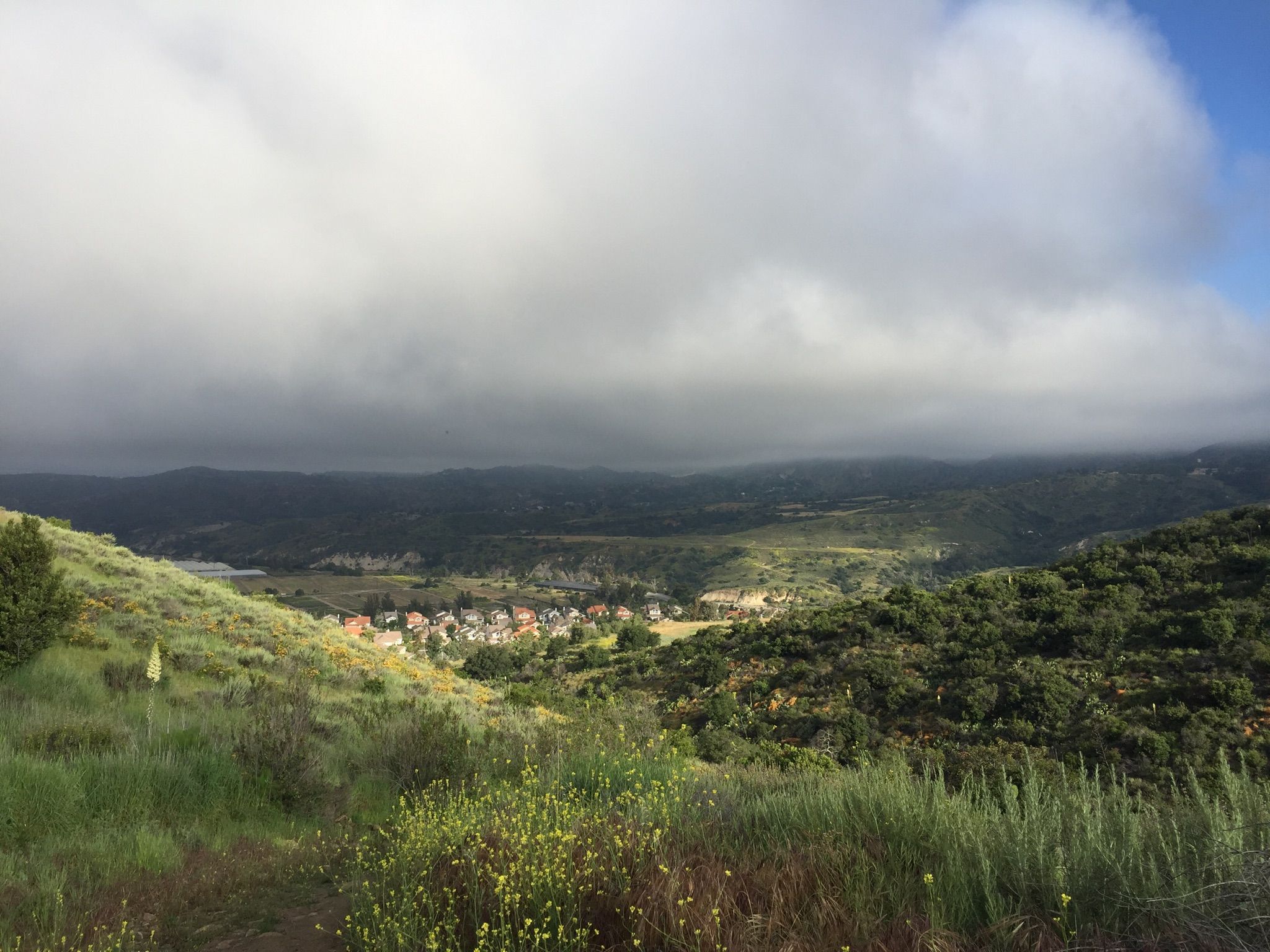 Green hills overlook a valley town under a dramatic, cloudy sky. - Bell View Trail Loop